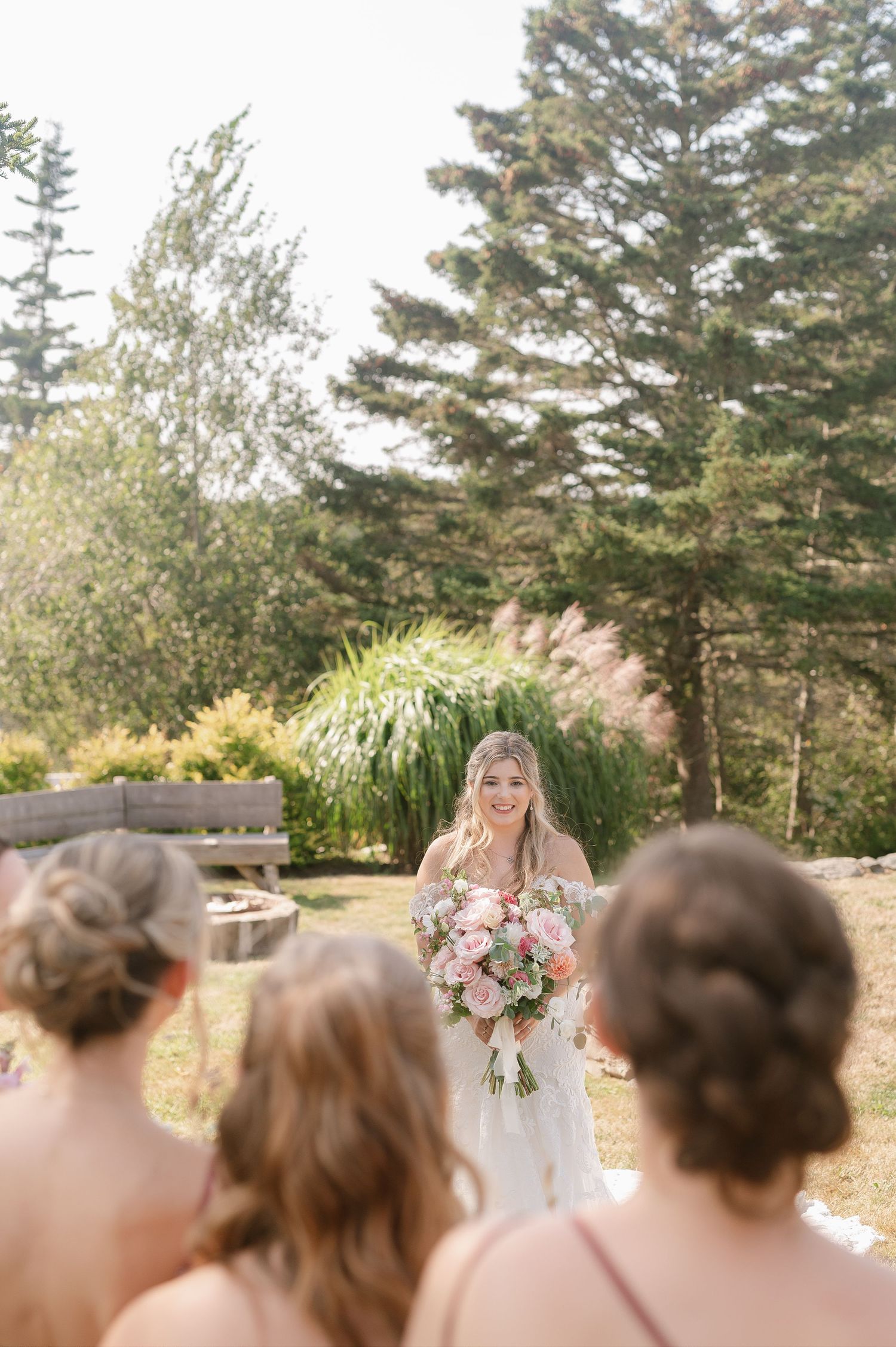Wedding party gathering outdoors with pine trees and natural sunlight.