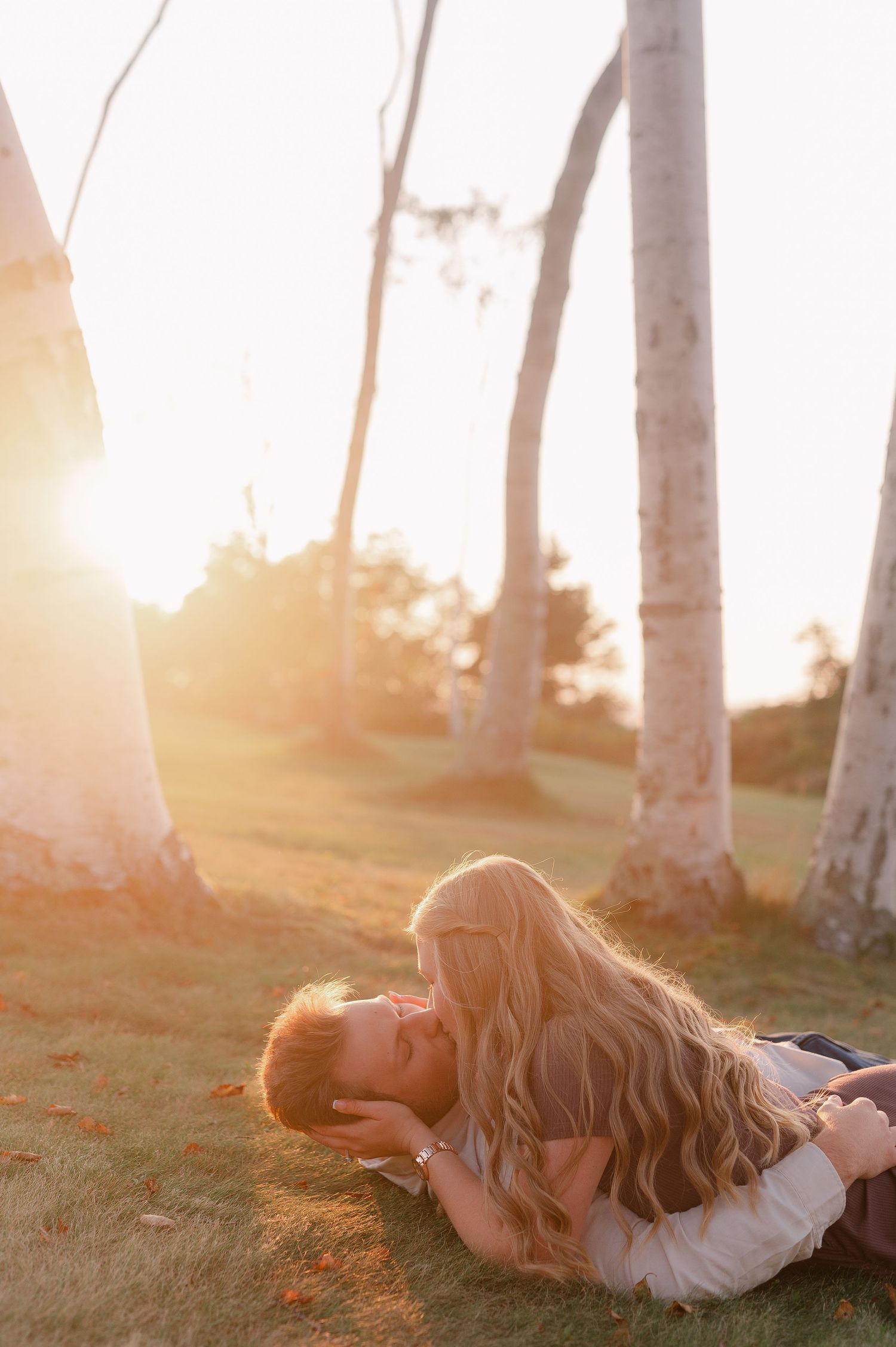 A person lies peacefully in white clothing among birch trees at sunset.