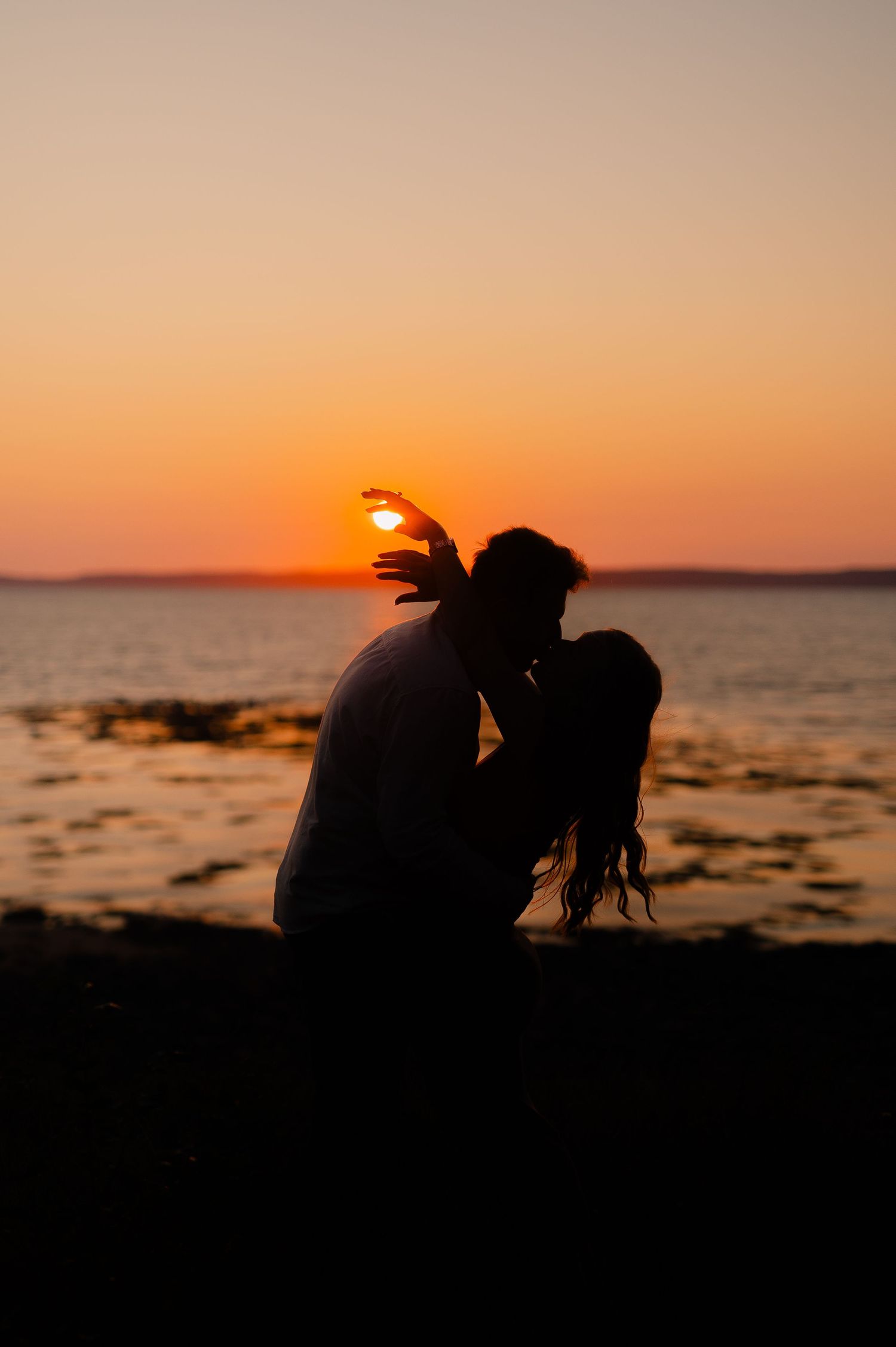 Silhouettes of a couple against a vibrant orange sunset over the ocean.