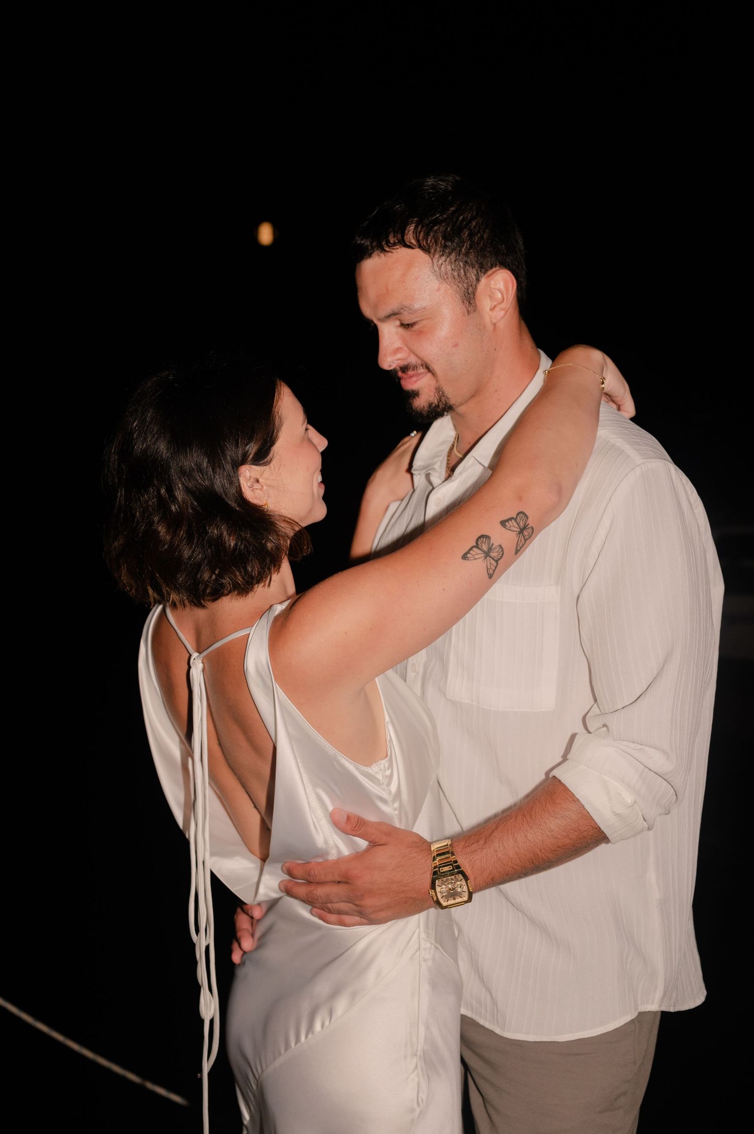 A romantic couple dancing together at night, dressed in white and embracing intimately.