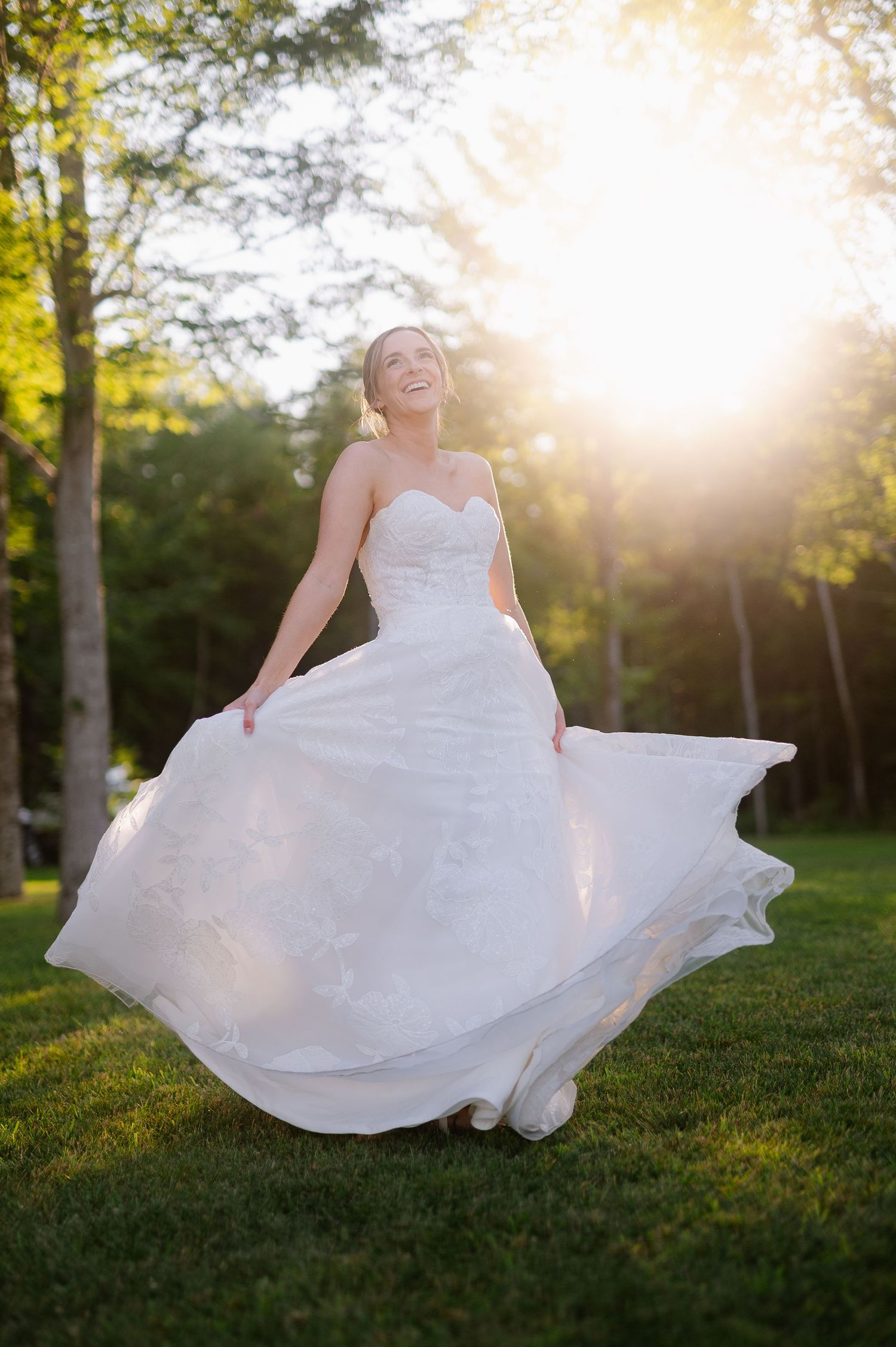 White wedding dress twirls gracefully in golden sunset light on grassy lawn.