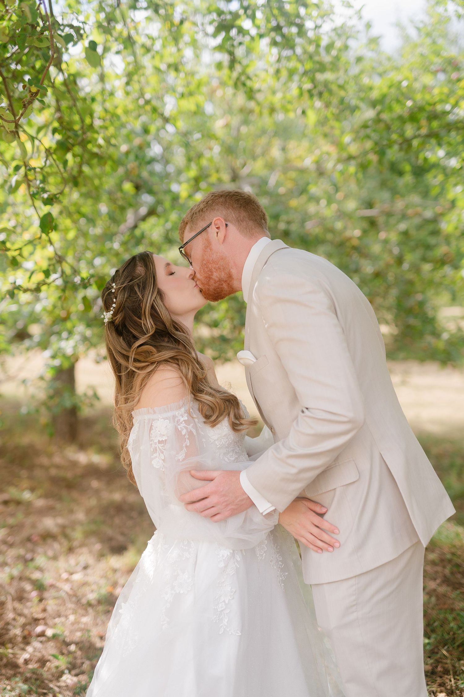 Romantic wedding portraits in a sunlit orchard with soft natural lighting.