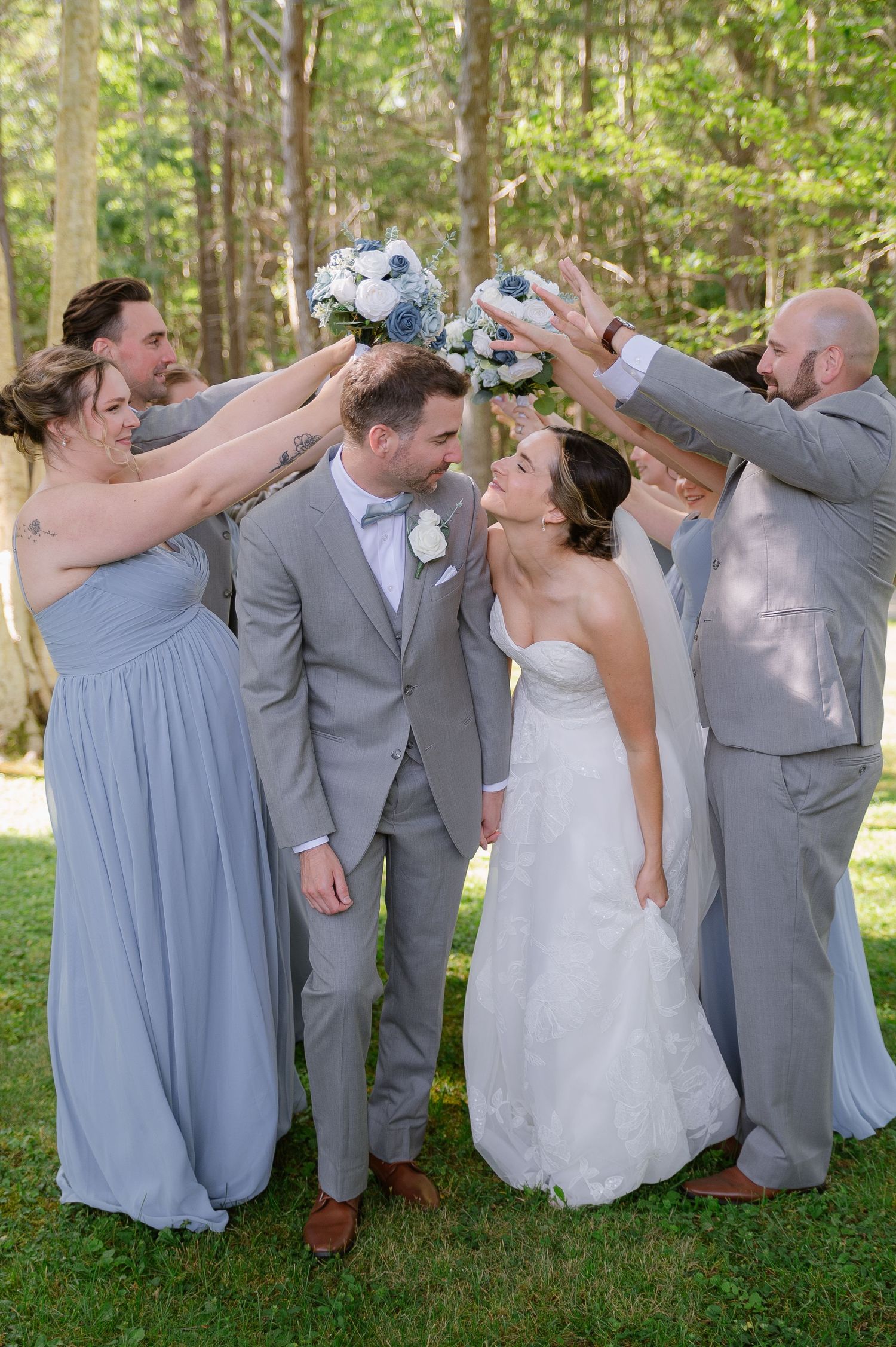 Wedding party in gray and blue attire poses playfully on grass.