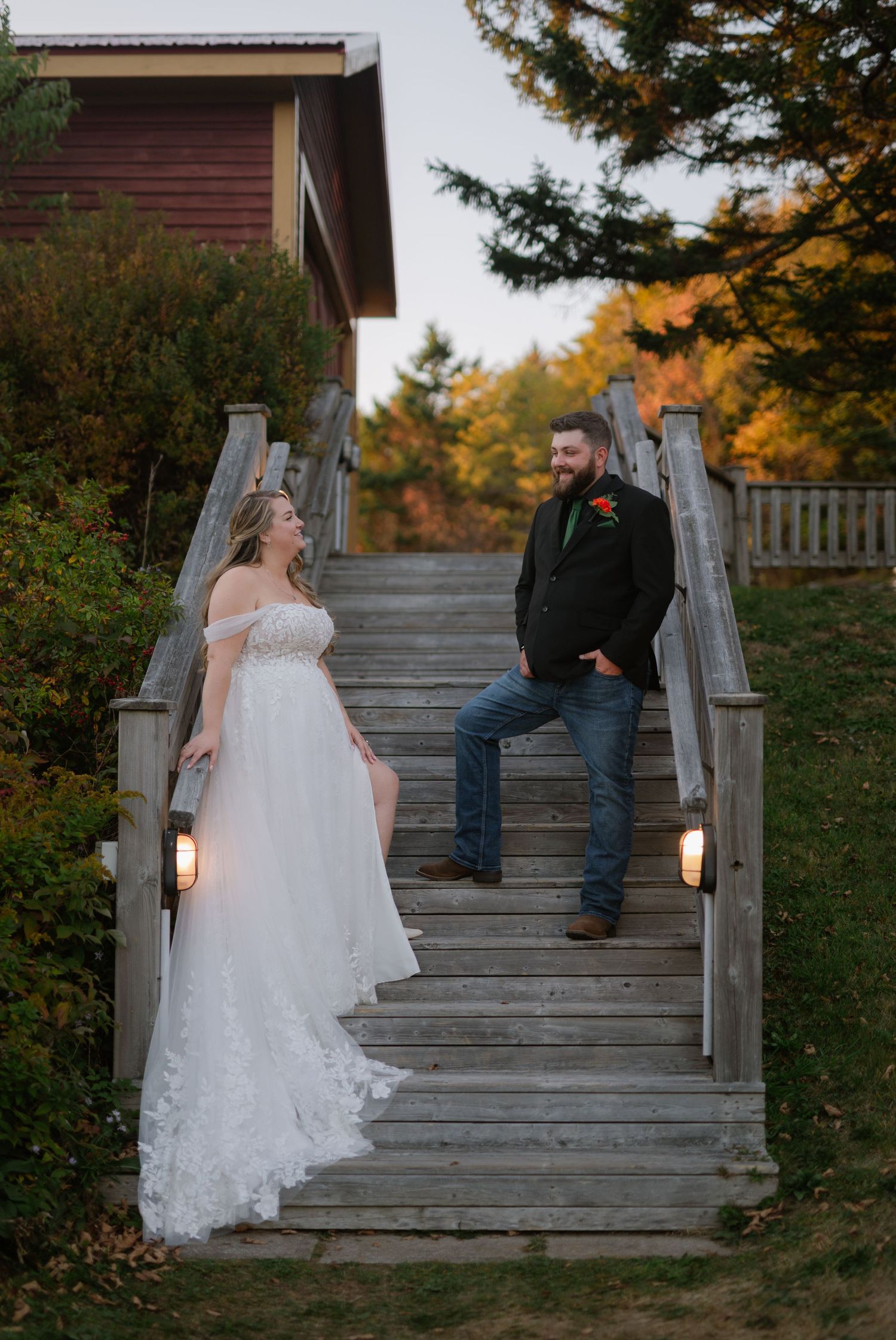 Wedding couple poses on rustic wooden stairs surrounded by autumn foliage.