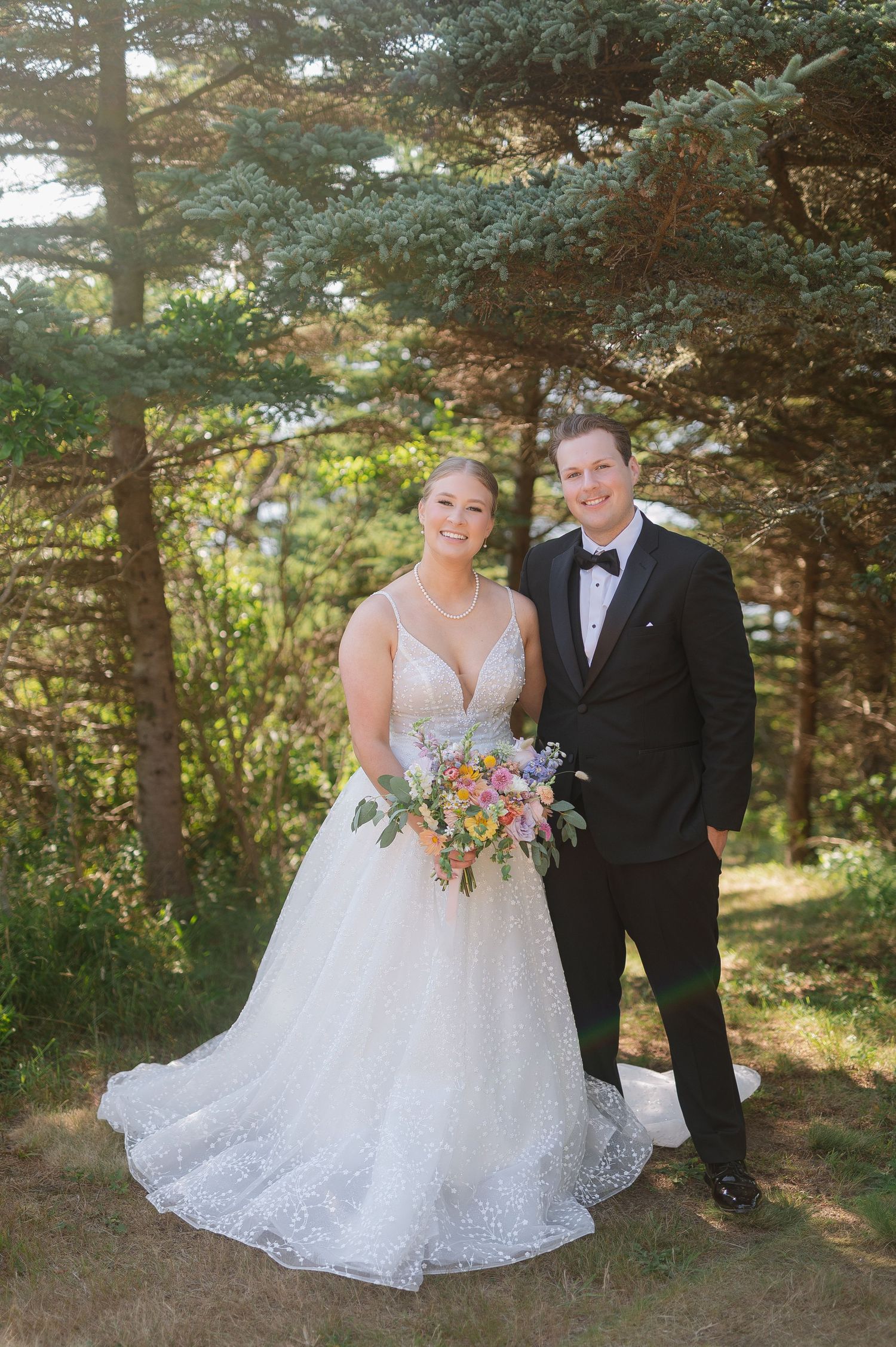 Elegant outdoor wedding portraits among pine trees with colorful floral bouquet.
