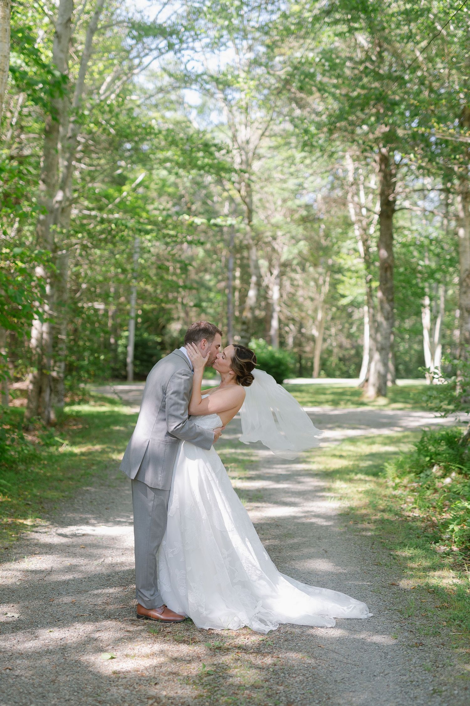 Wedding couple shares intimate moments on a tree-lined path in an outdoor setting.