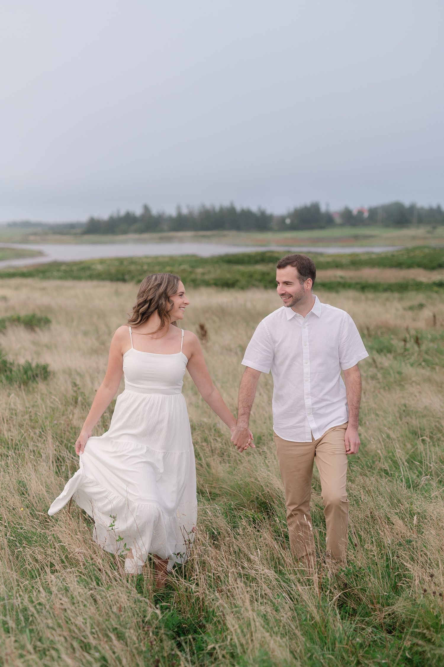 Couple walking hand in hand through tall grass near the coast.