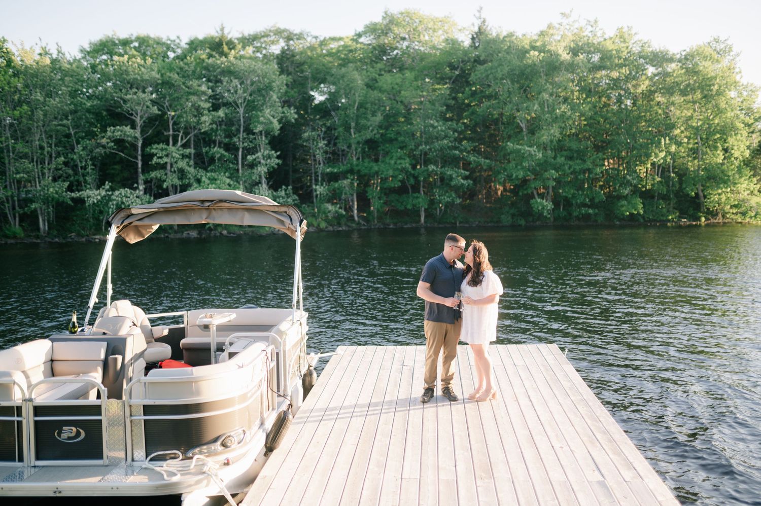 Romantic lakeside photo session on a wooden dock with boat and trees in background.