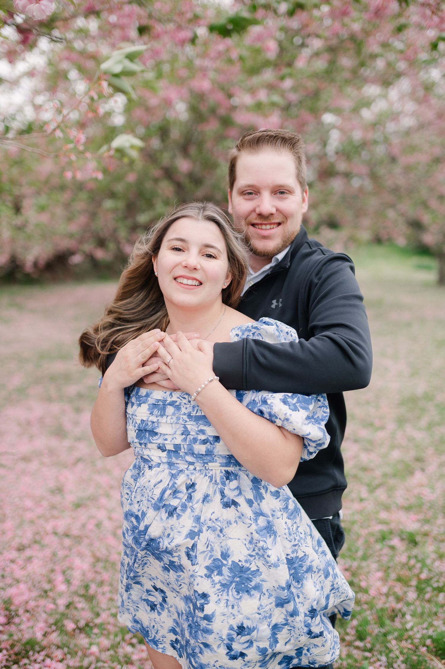 Playful couple photoshoot among blooming pink cherry blossoms in spring.