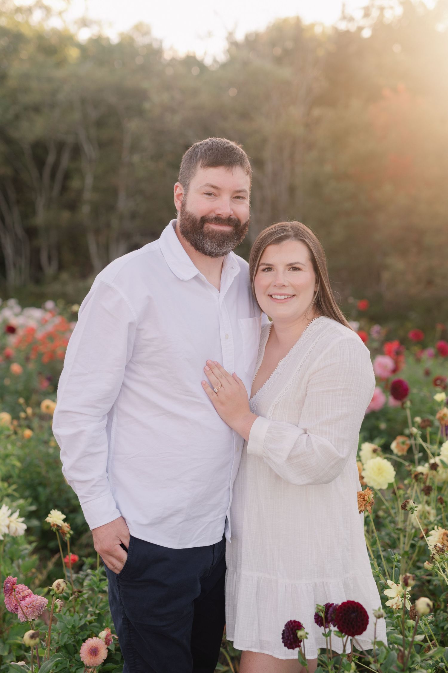 Couple in white clothing sharing a joyful moment in a dahlia garden at sunset.