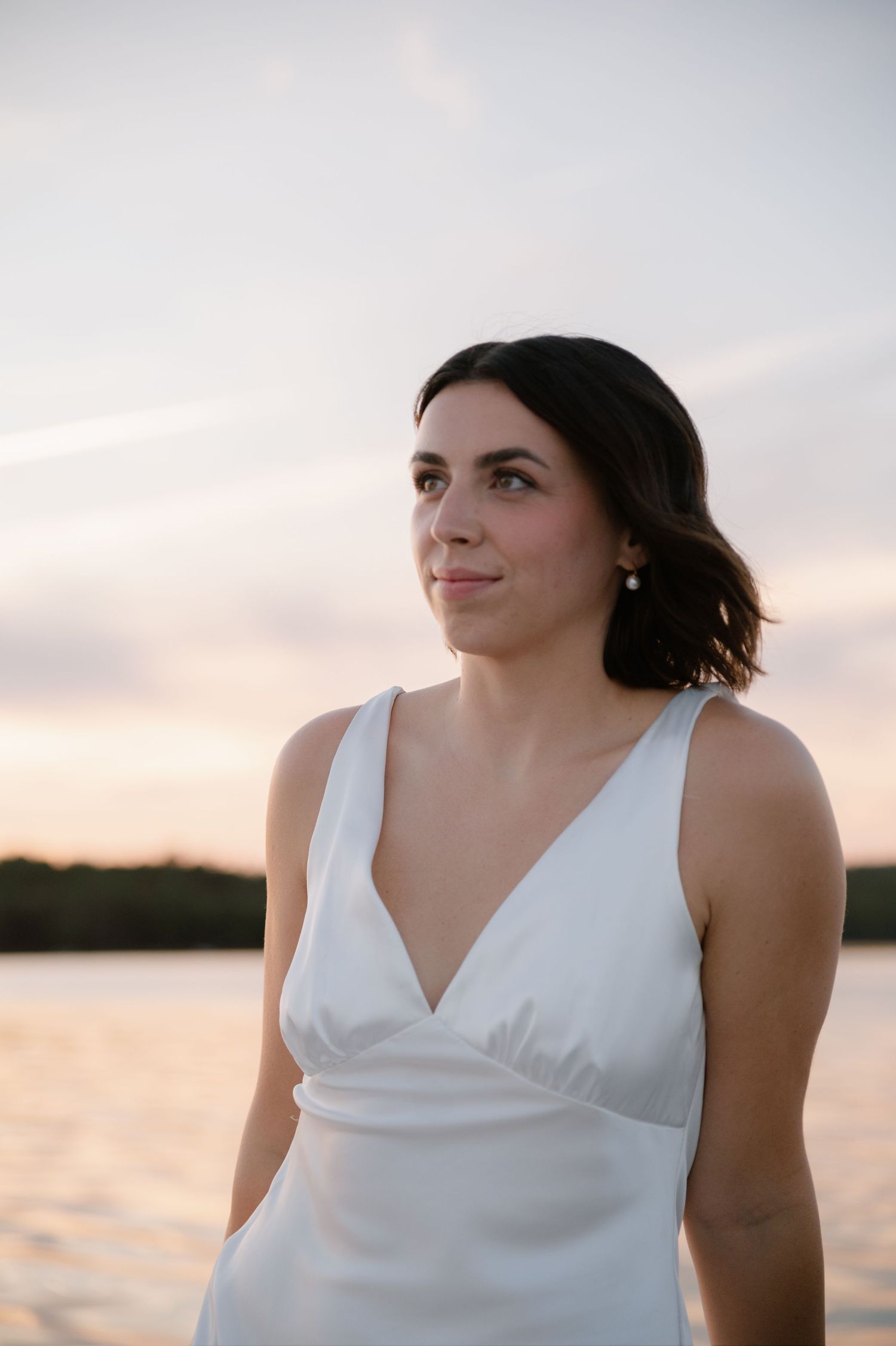 Woman in white dress poses on sailboat during golden hour with water backdrop.
