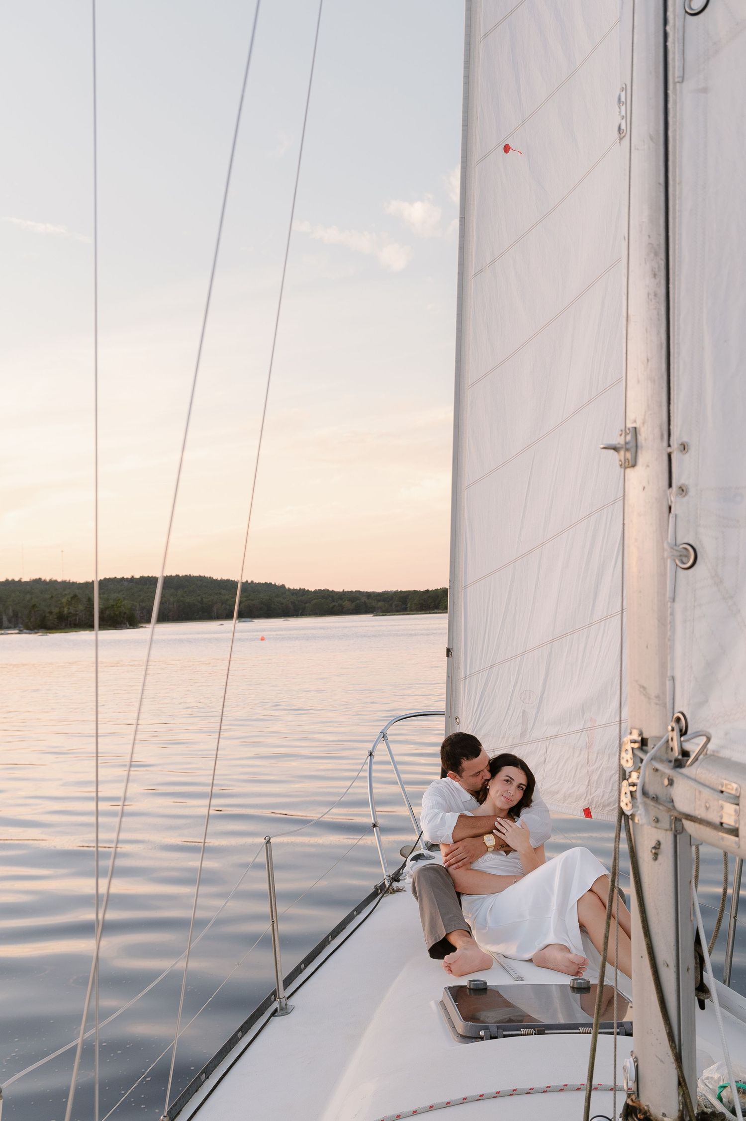 A romantic moment captured on a sailboat with white sails and calm waters in the background.