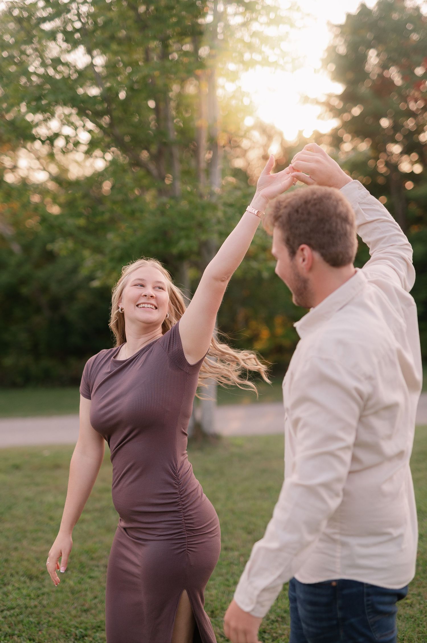 A couple dances playfully in a grassy field during golden hour.