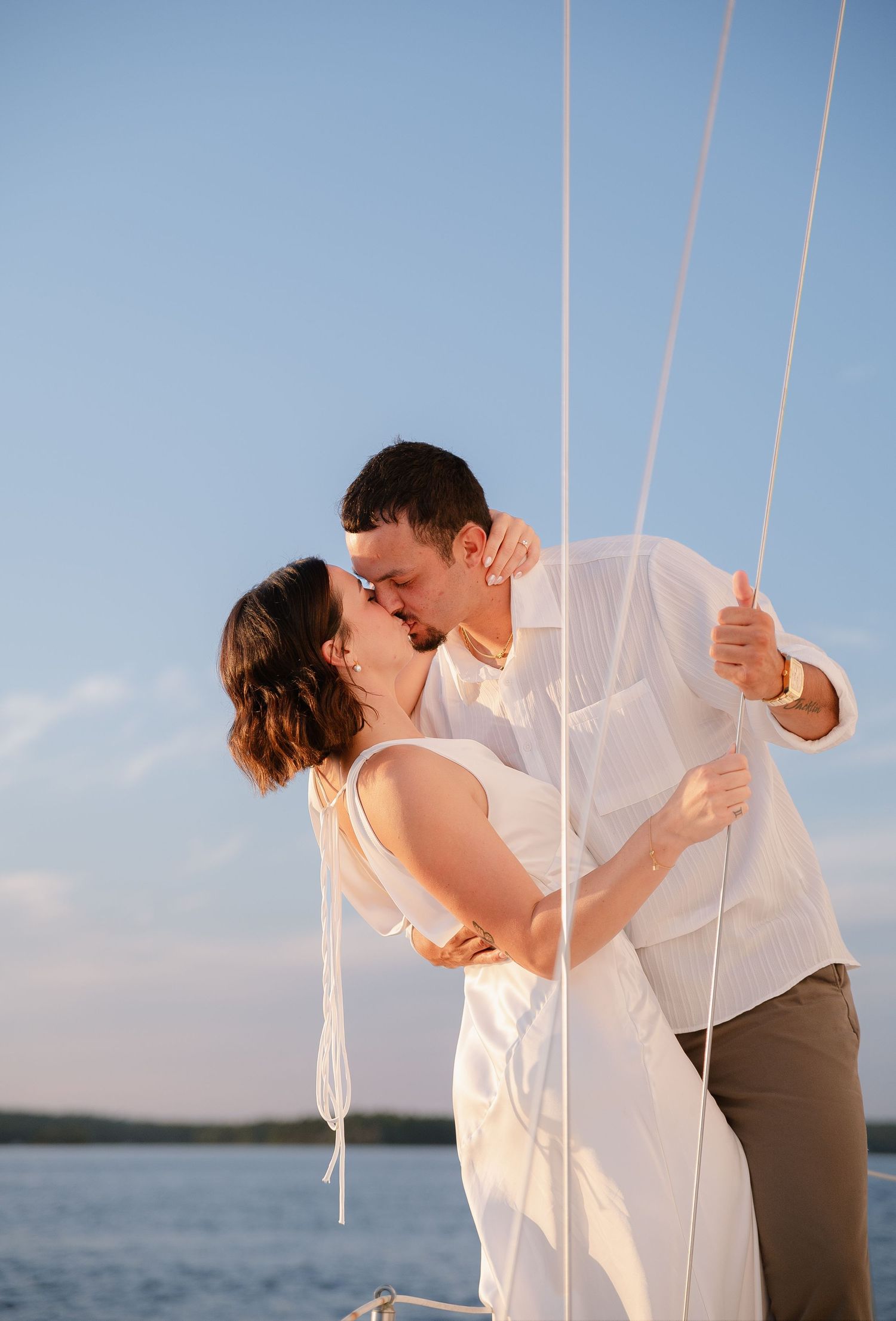 A couple embraces near sailing ropes on a boat deck during a sunny day.