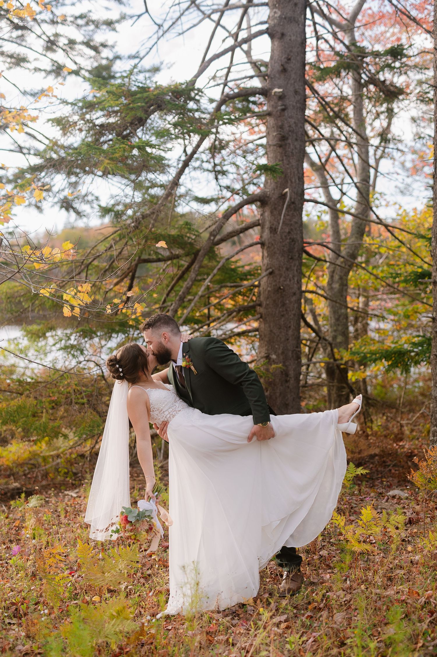 Wedding couple poses romantically among pine trees in an autumn forest setting.