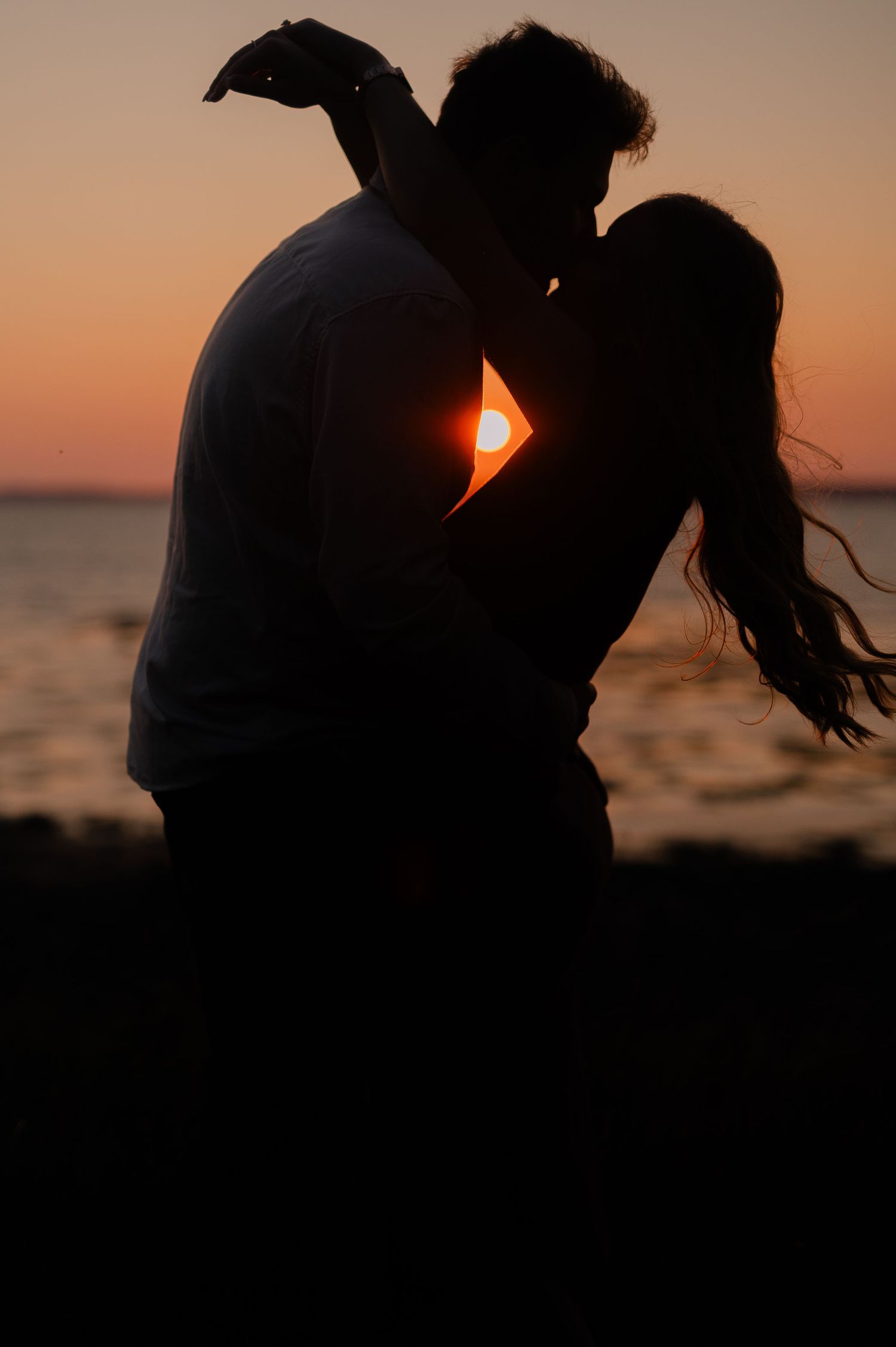 Romantic silhouettes share an intimate moment at sunset by the water.