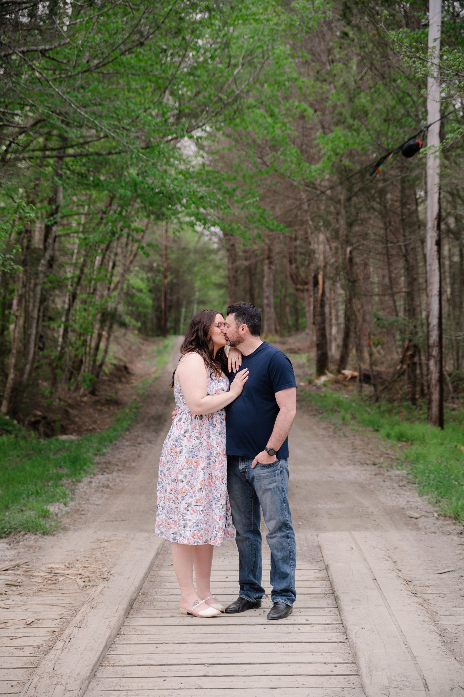 Couple sharing intimate moments on wooden boardwalk surrounded by trees.