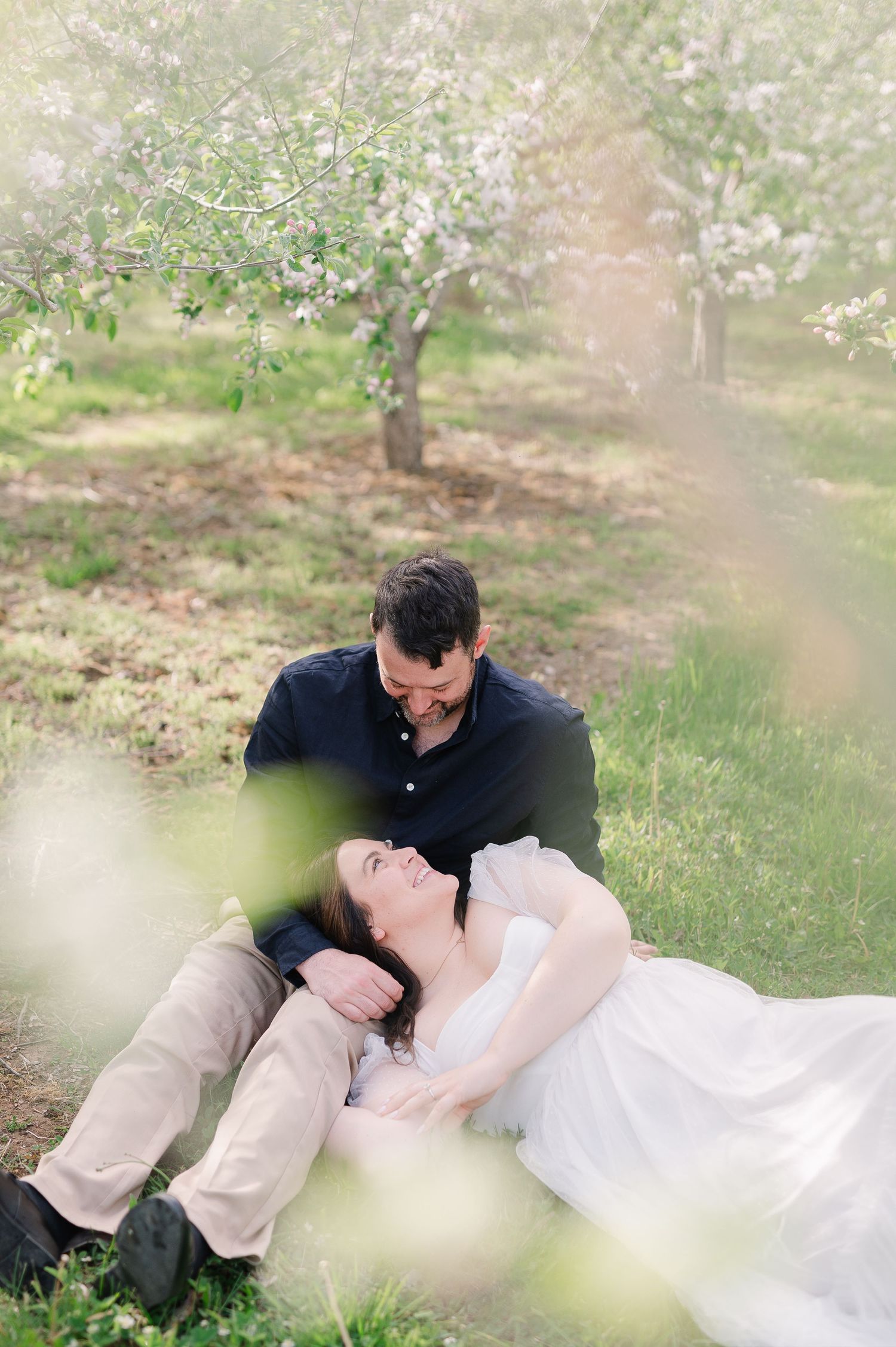 Couple laying on grass during springtime photo session with blossoming trees.