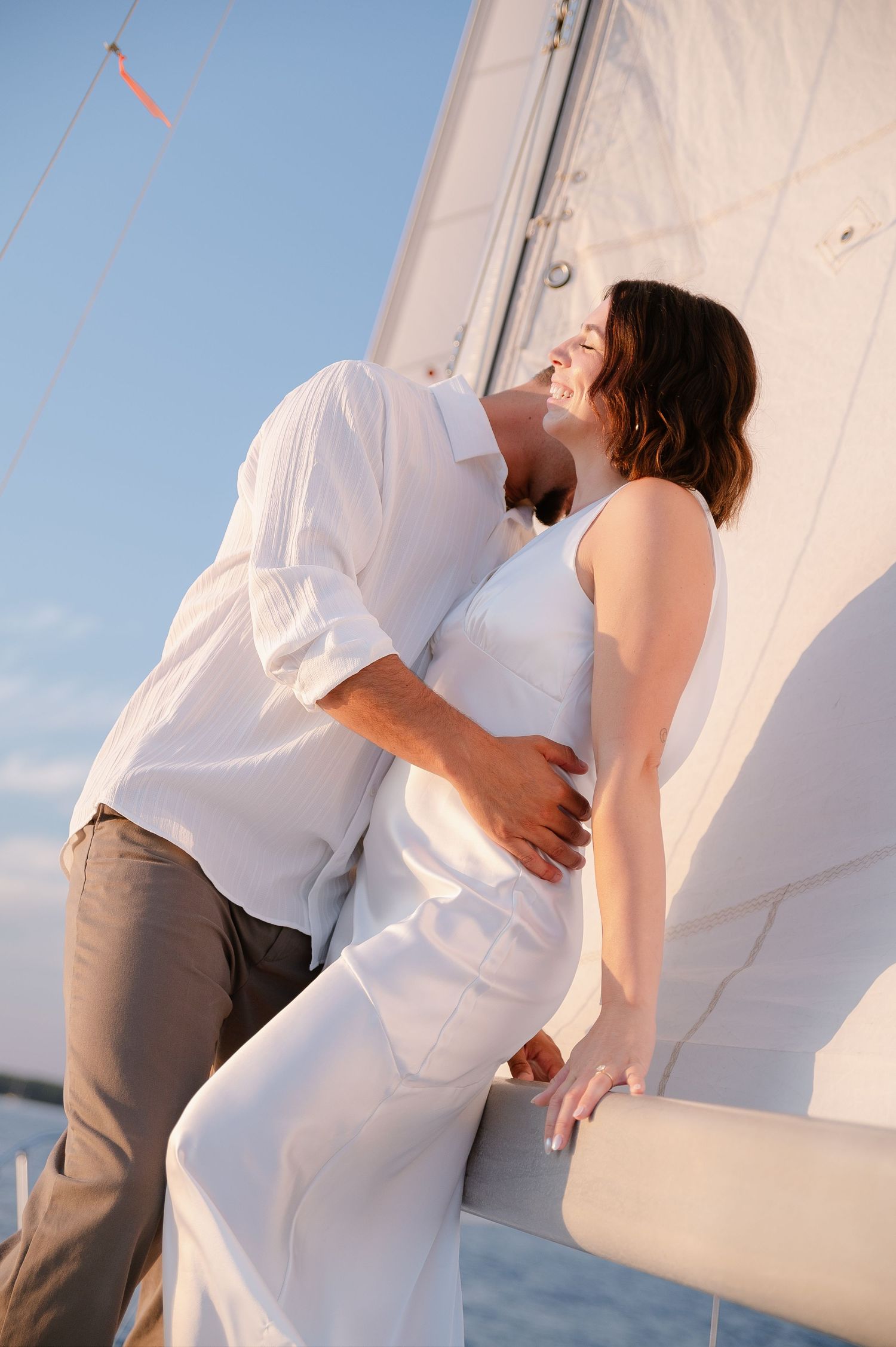 Intimate moments shared between a couple in white and beige attire on a sailboat deck.