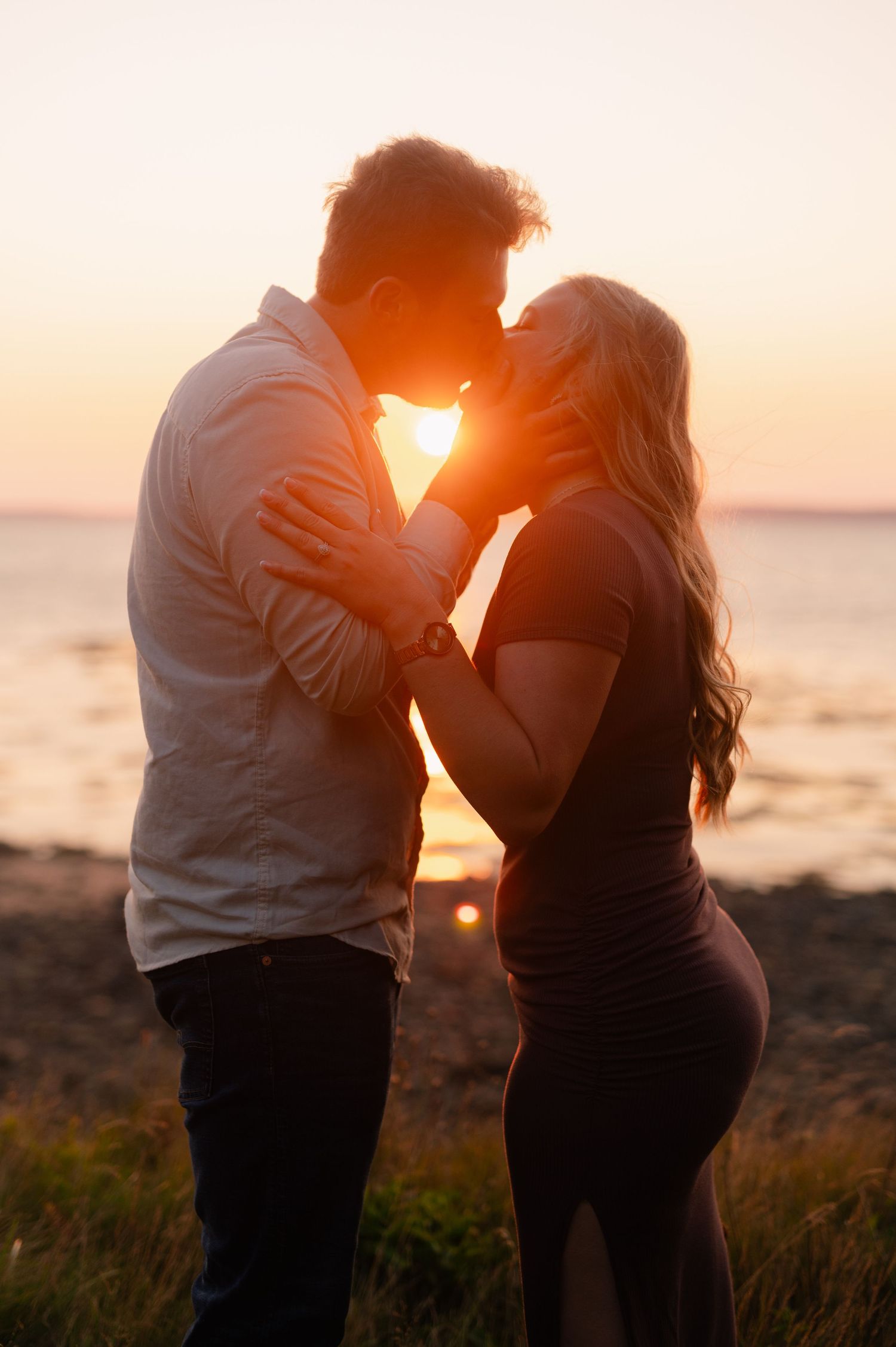 A couple shares an intimate moment silhouetted against a dramatic sunset over the ocean.