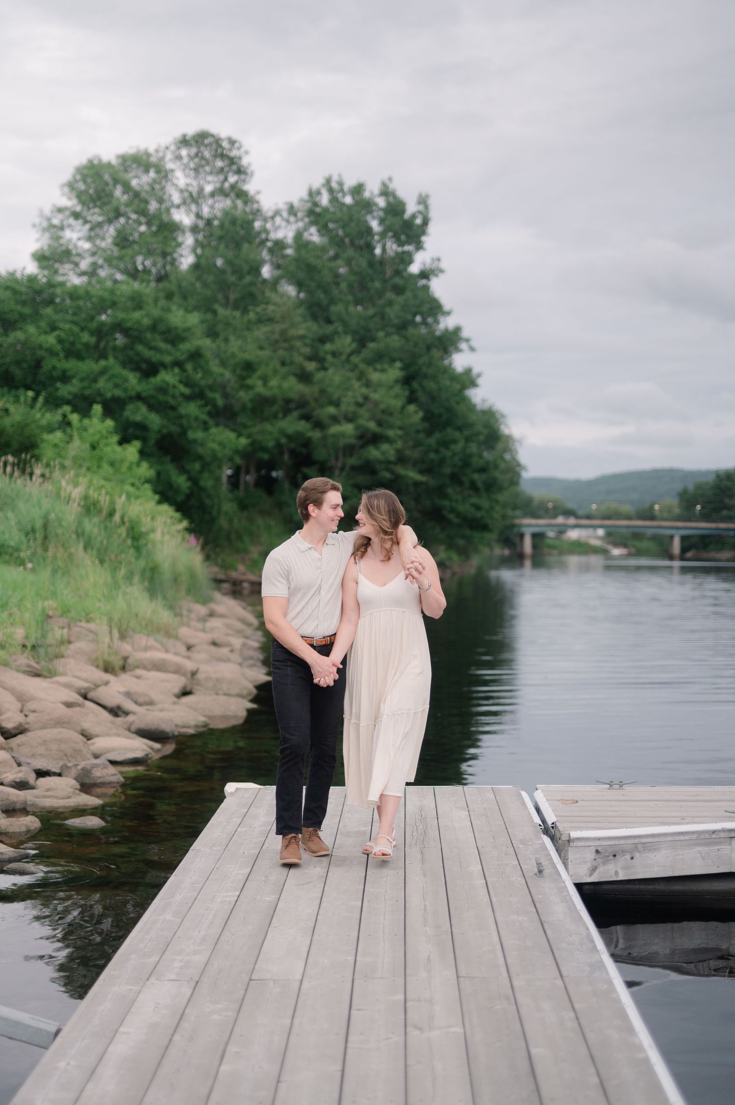 Two people share an intimate moment while sitting on a wooden dock by the water.