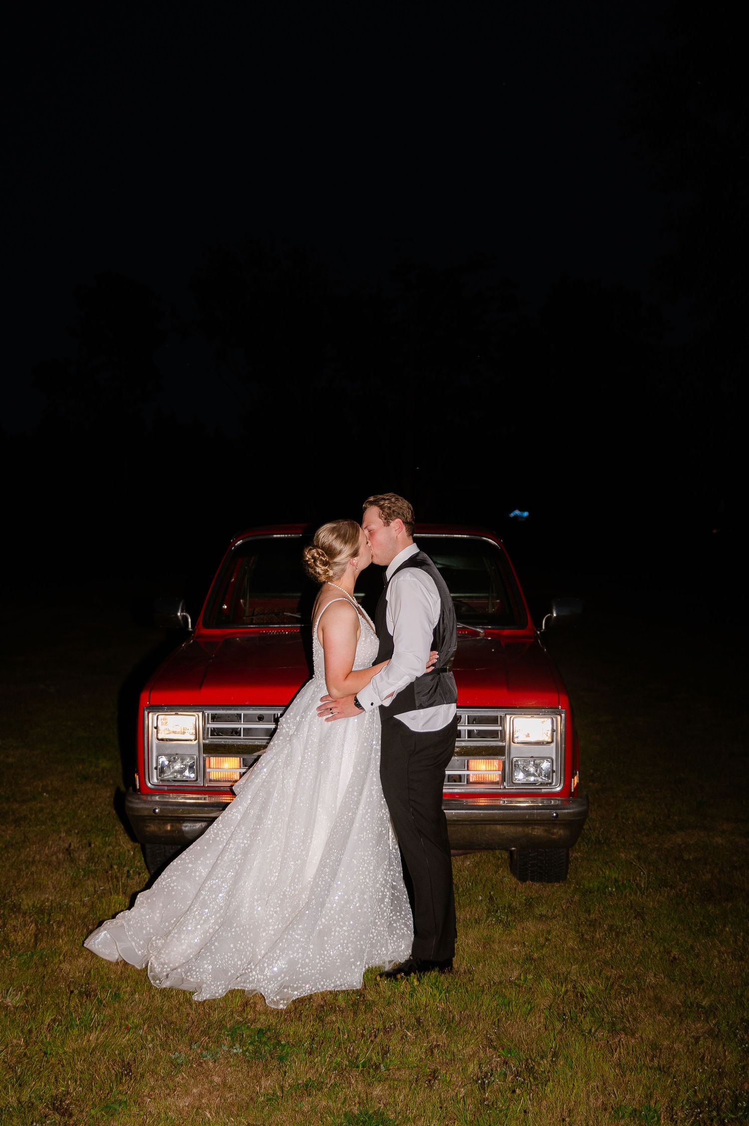 Romantic nighttime wedding photos with vintage red car illuminated in background.