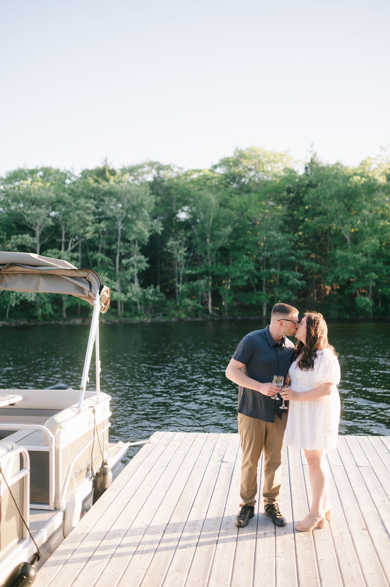 Couple embracing on a wooden dock by a serene lake surrounded by trees.