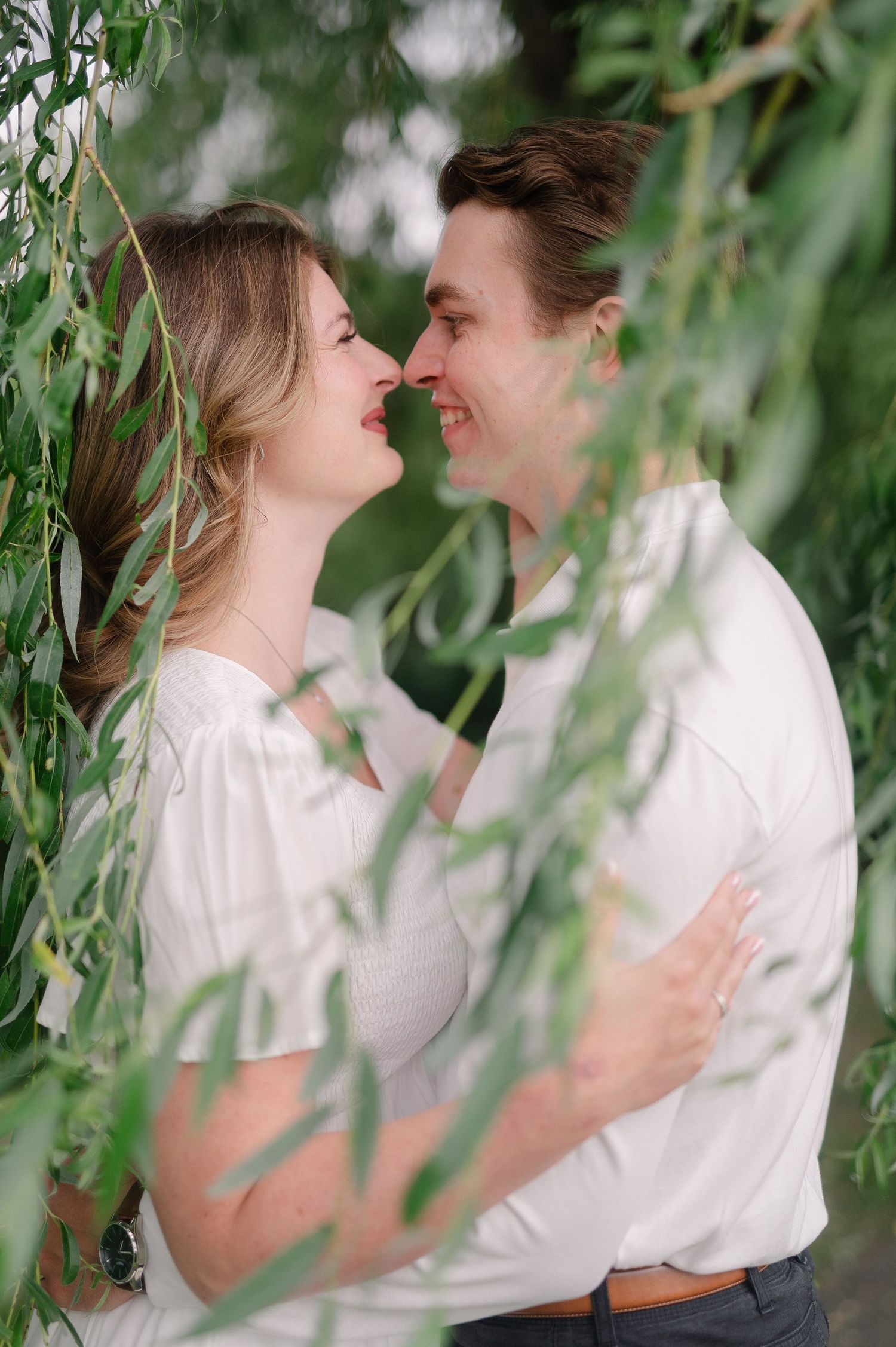A romantic moment framed by hanging willow branches in soft natural light.