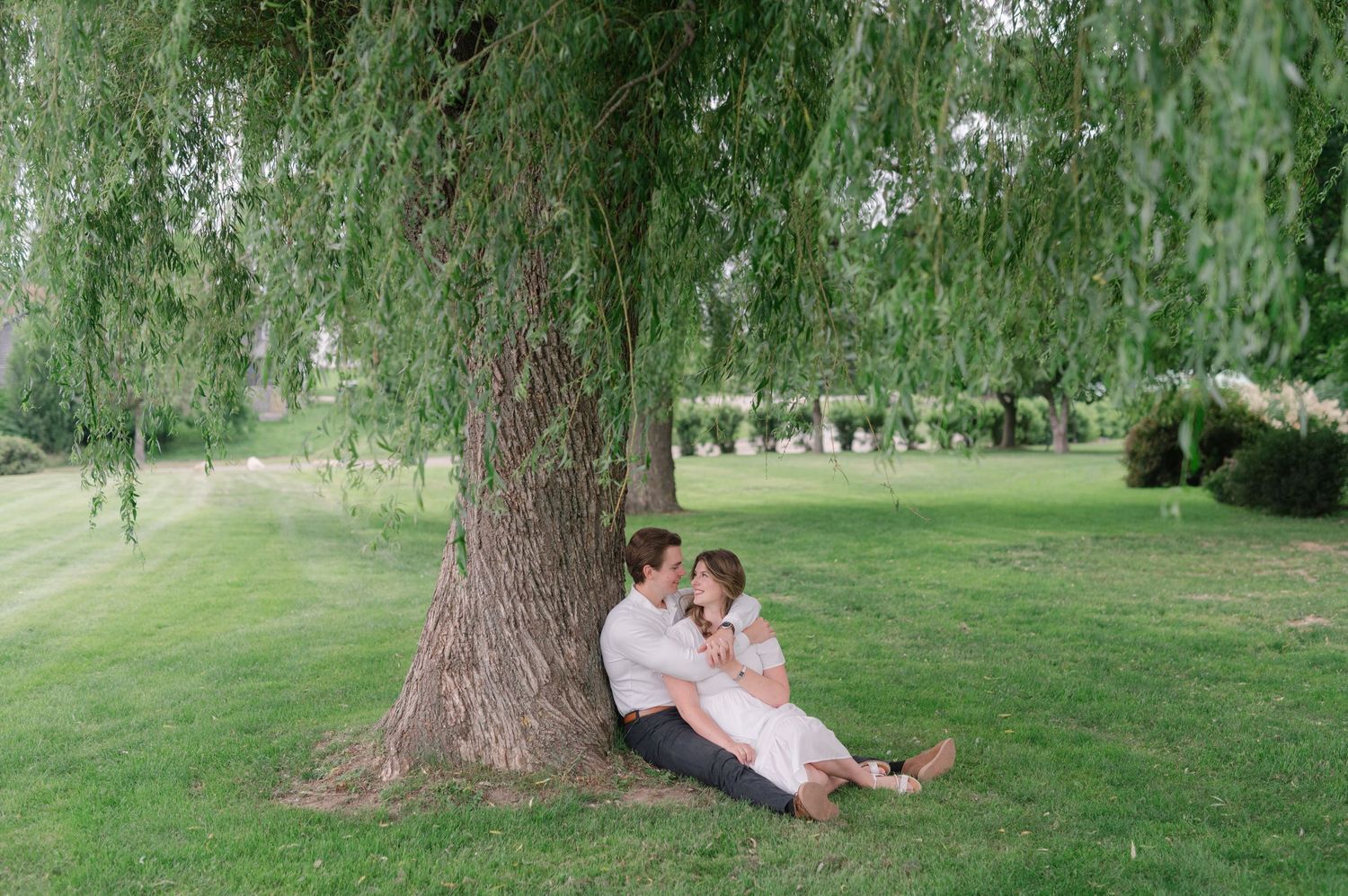 Couple relaxing together under a large willow tree in a park setting.