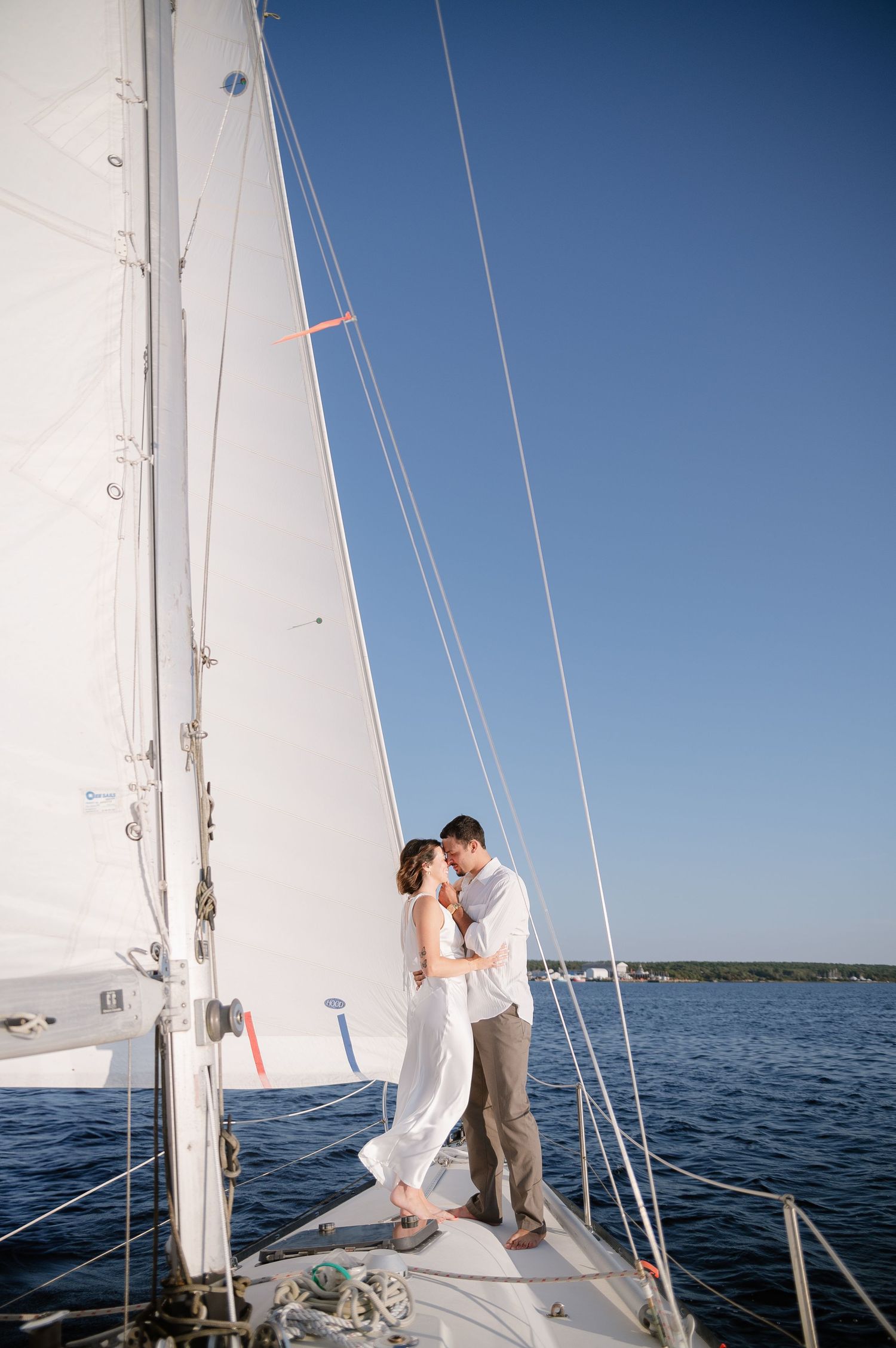 Romantic sailing photoshoot with a couple against clear blue skies and white sails.