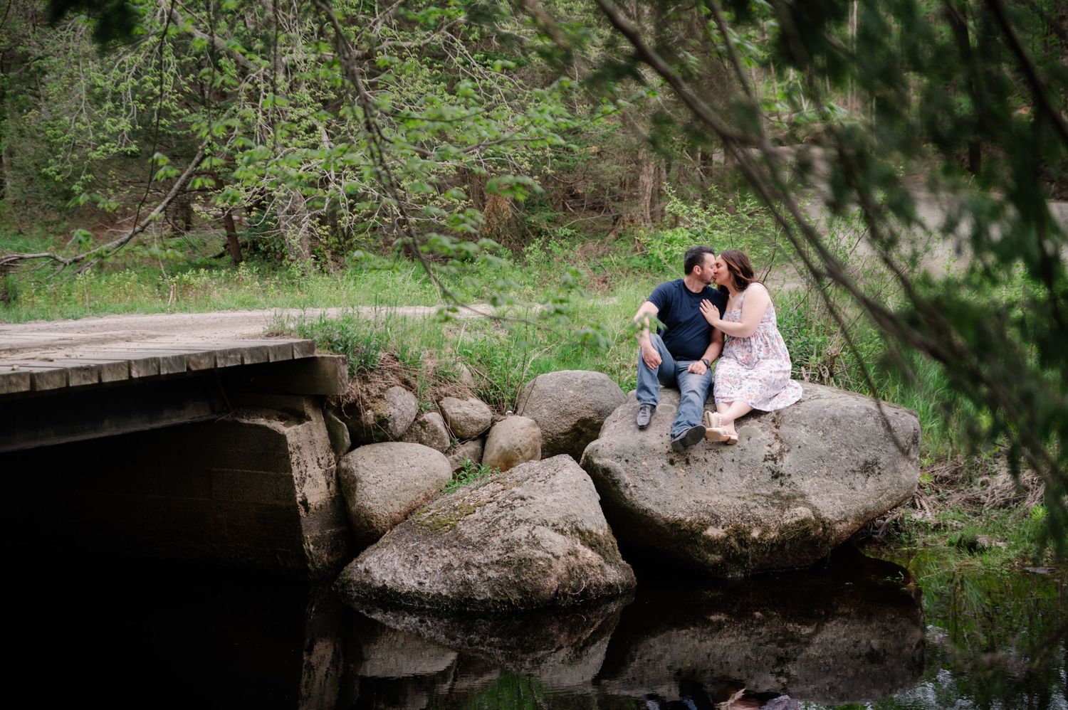 Couple sitting on large rocks near water during outdoor photo session.
