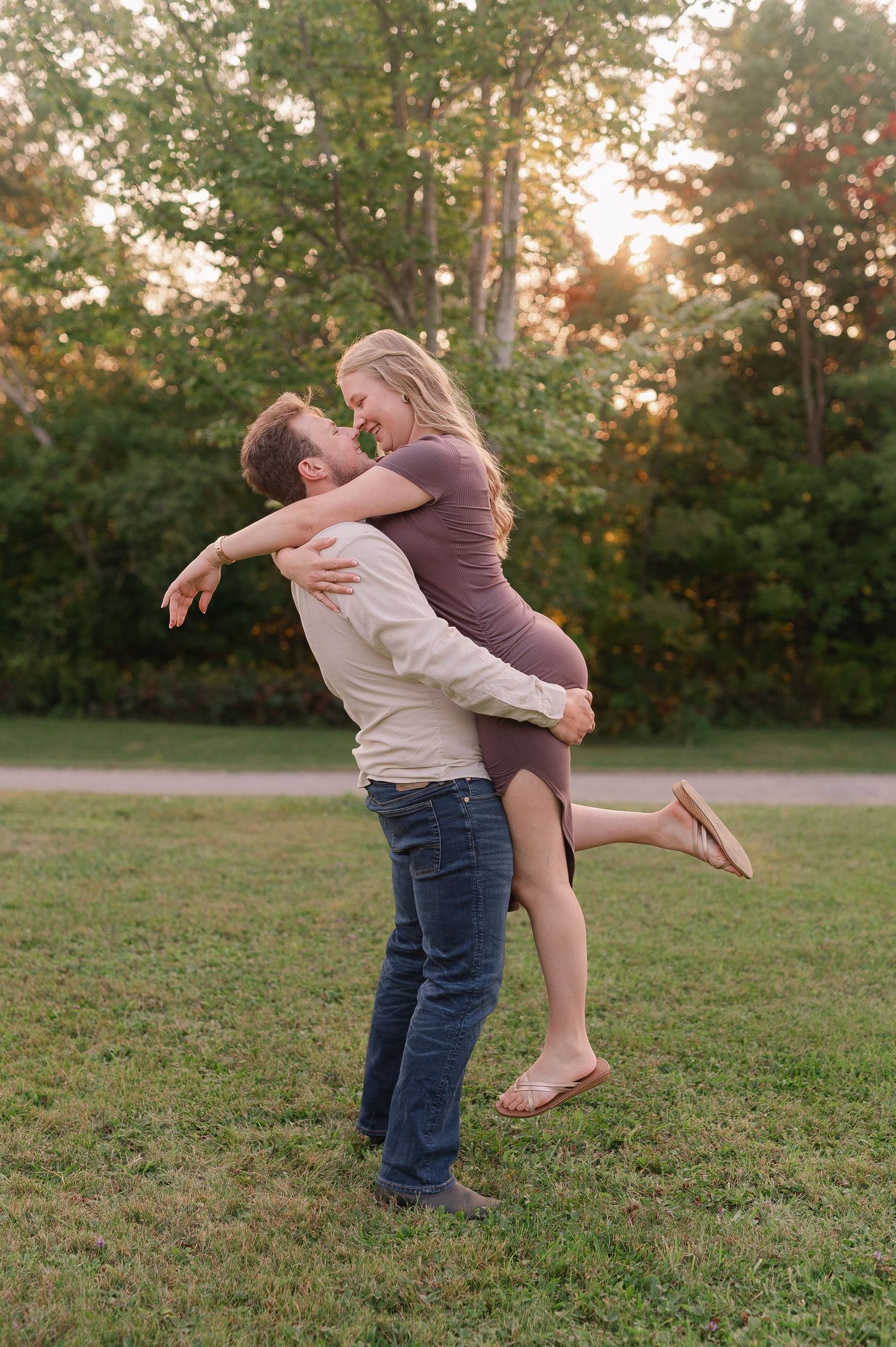 A playful couple spins and embraces on a grassy lawn at sunset.