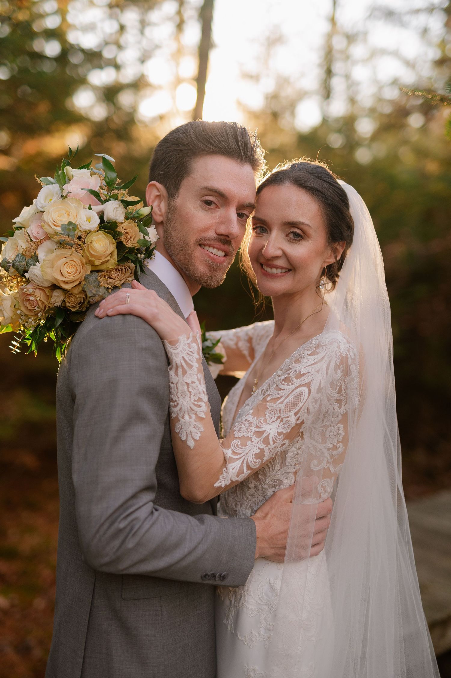 A joyful wedding portrait with soft autumn lighting and peach floral bouquet accents.