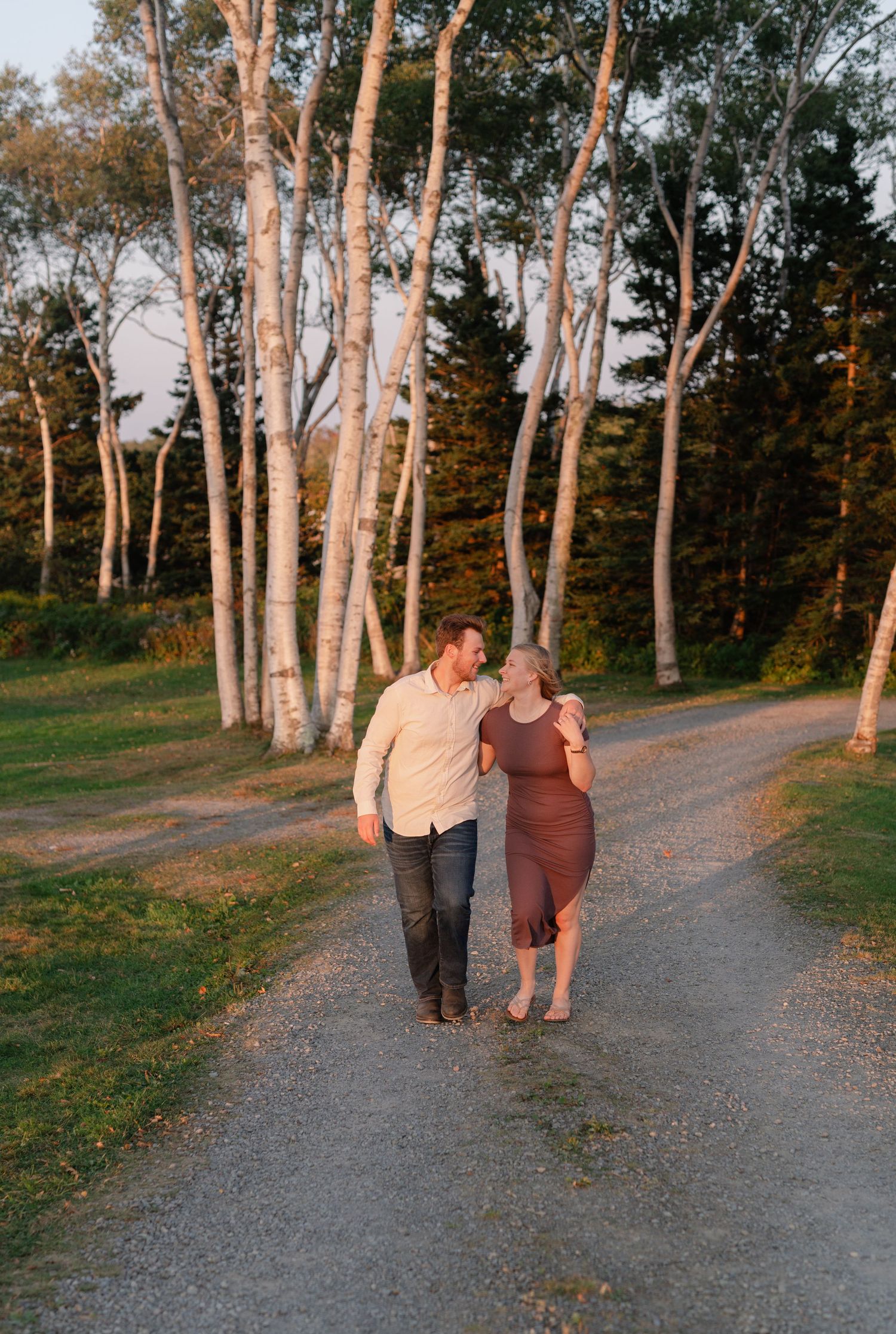 A couple walks hand in hand along a tree-lined path at sunset.