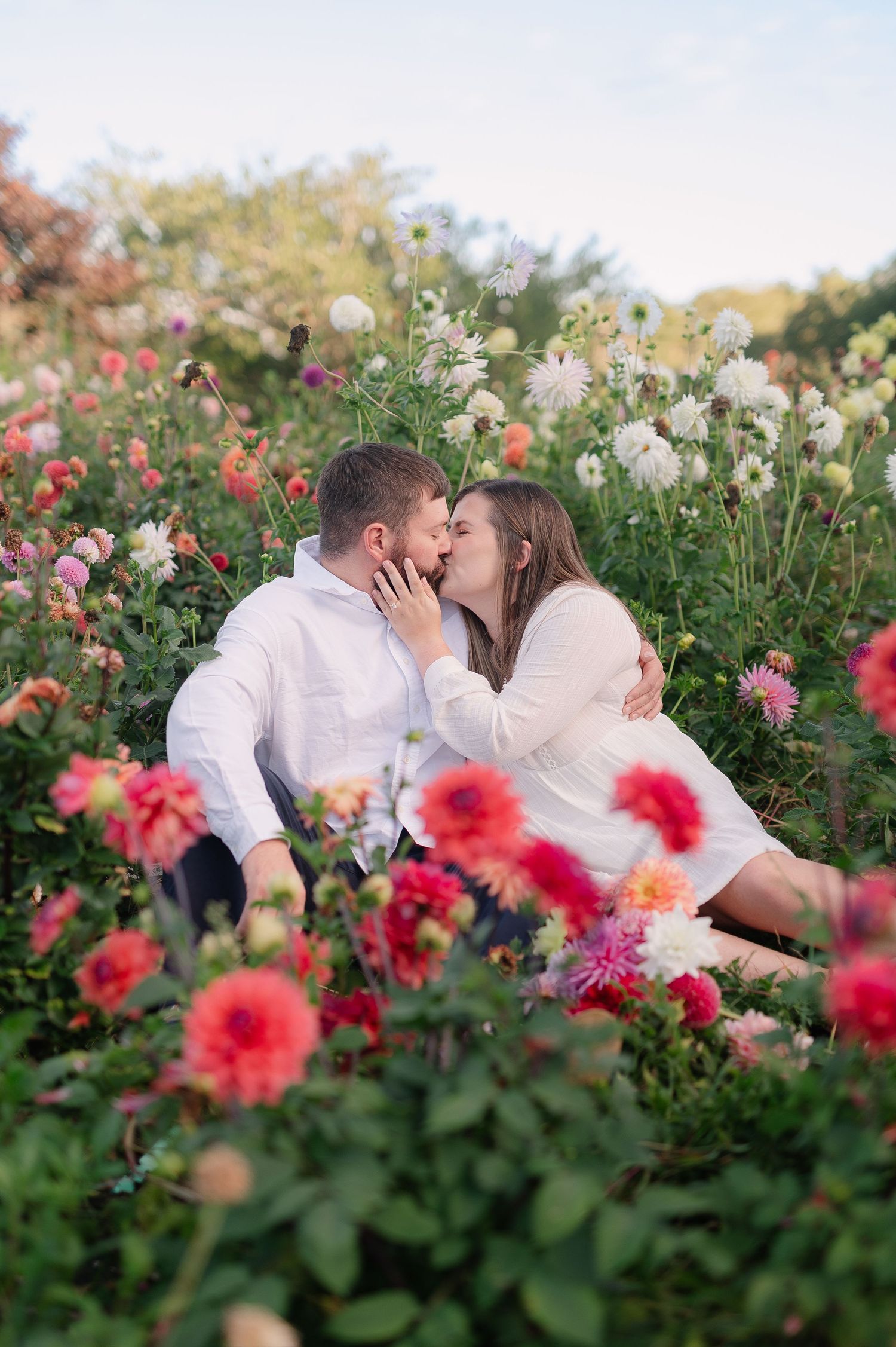 Intimate moment shared between couple among blooming dahlias and flowers at sunset.