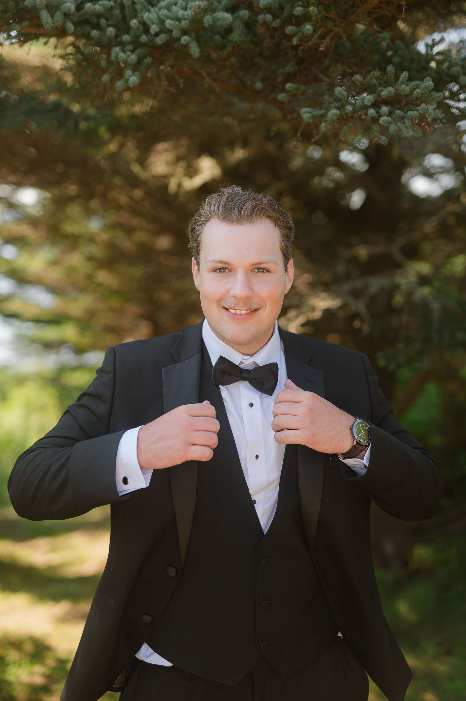 Formal black tuxedo with bow tie shown in outdoor wedding photography setting.