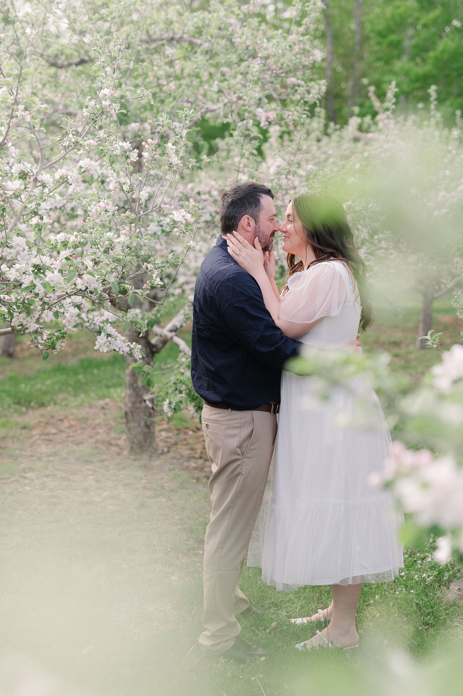 A romantic photoshoot in a blooming spring orchard with white blossoms in the background.