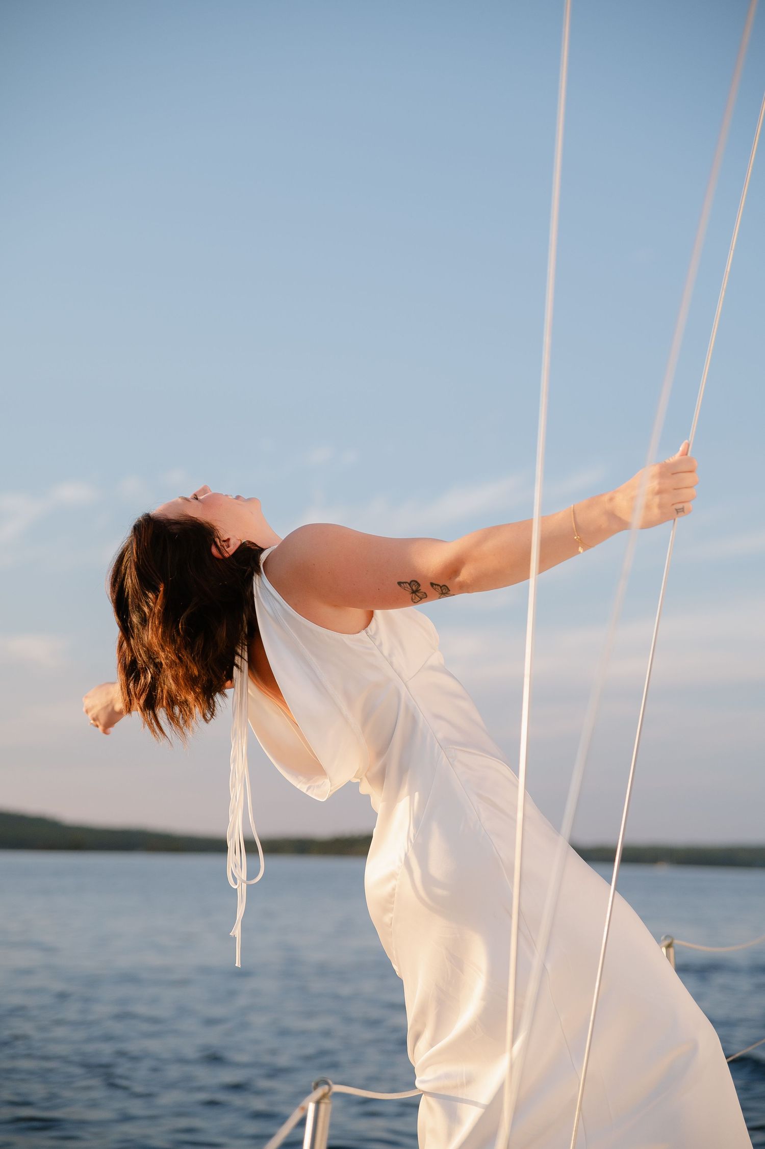 Person in white dress leaning back on a boat against a bright blue ocean backdrop.
