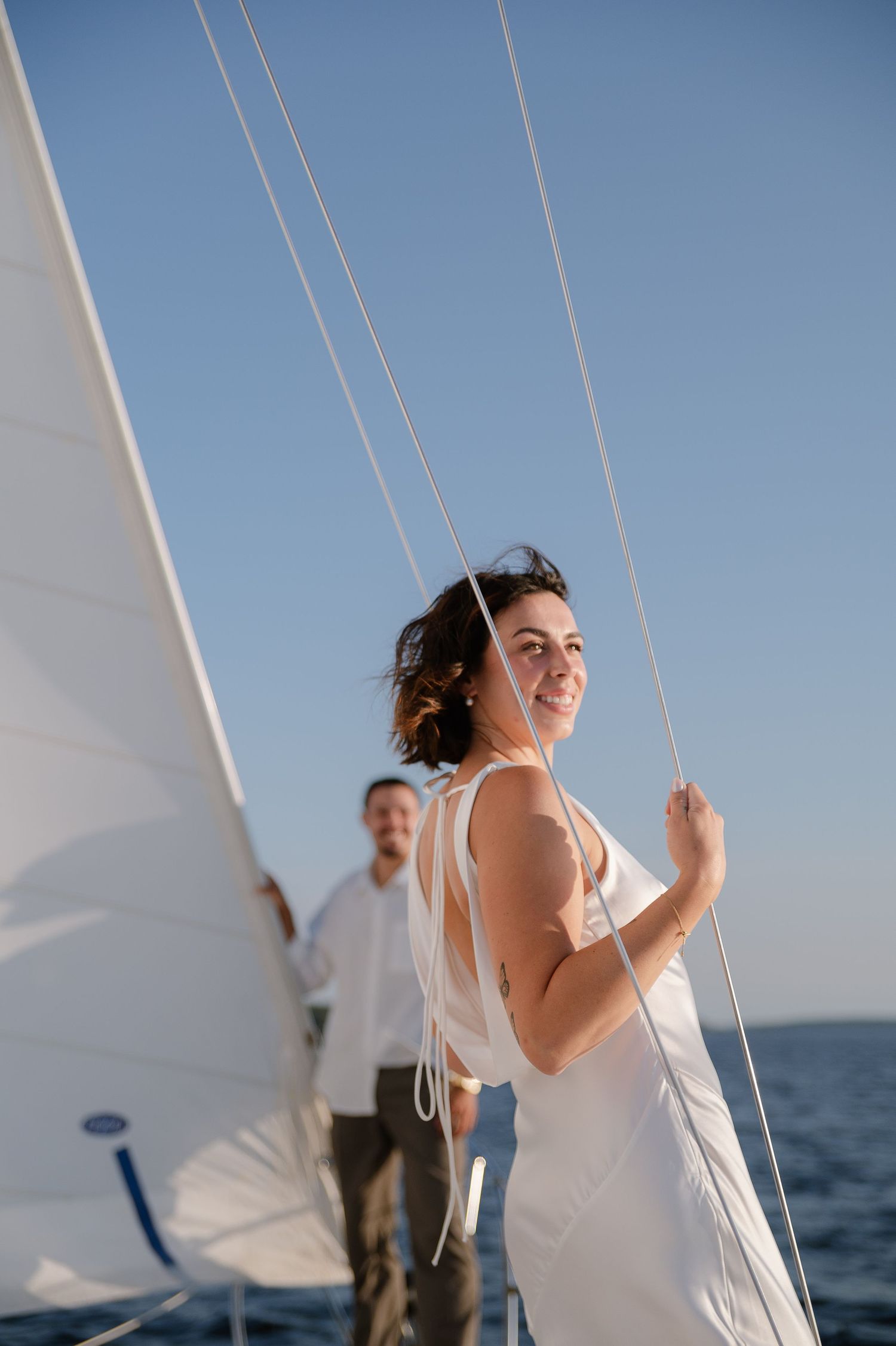 A couple in white attire shares romantic moments on a sailboat against a blue sky backdrop.