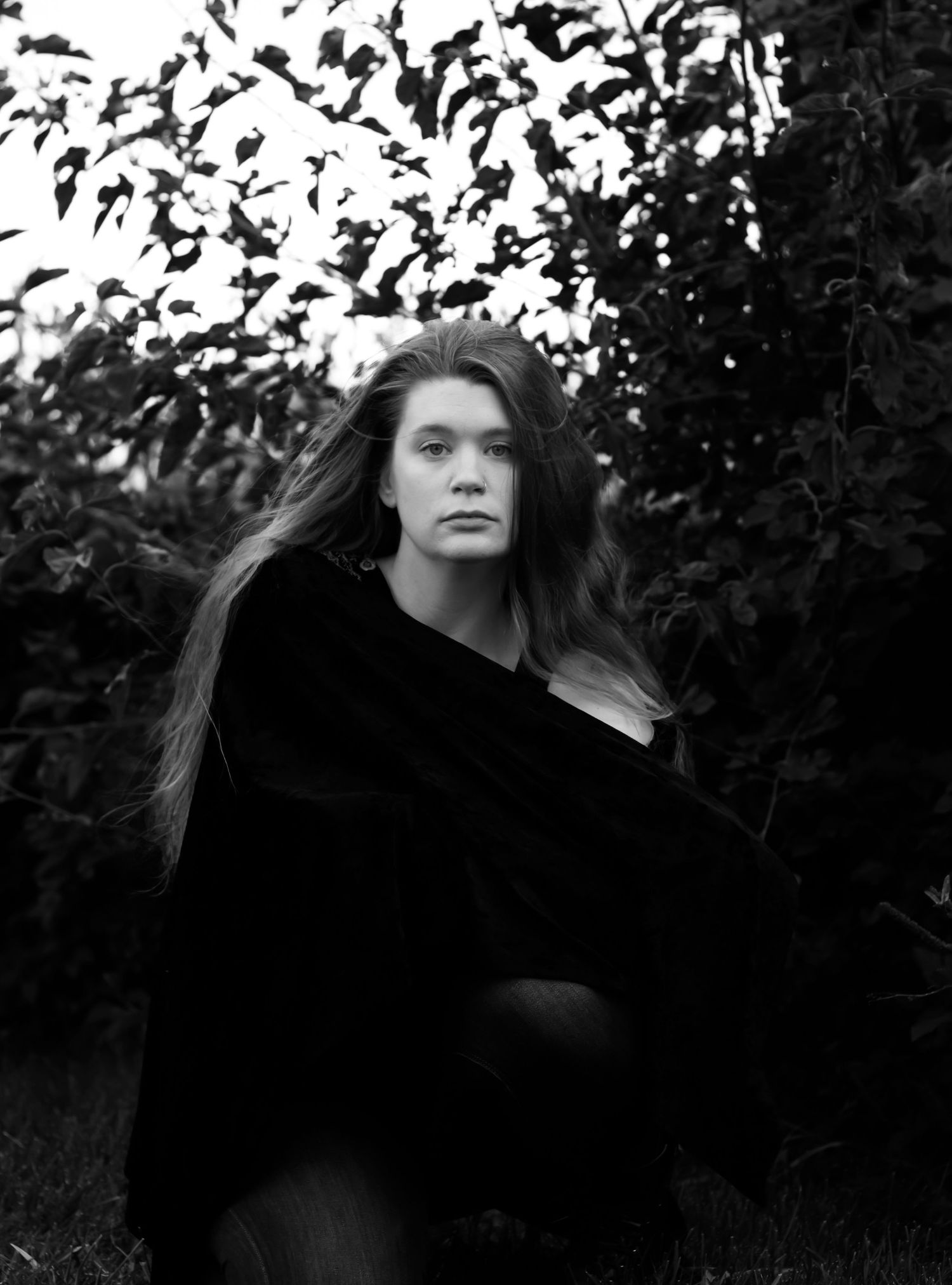 Black and white portrait photograph showing Bree of Sixtwentytwo Images wearing a dark sweater against a natural background with leaves.