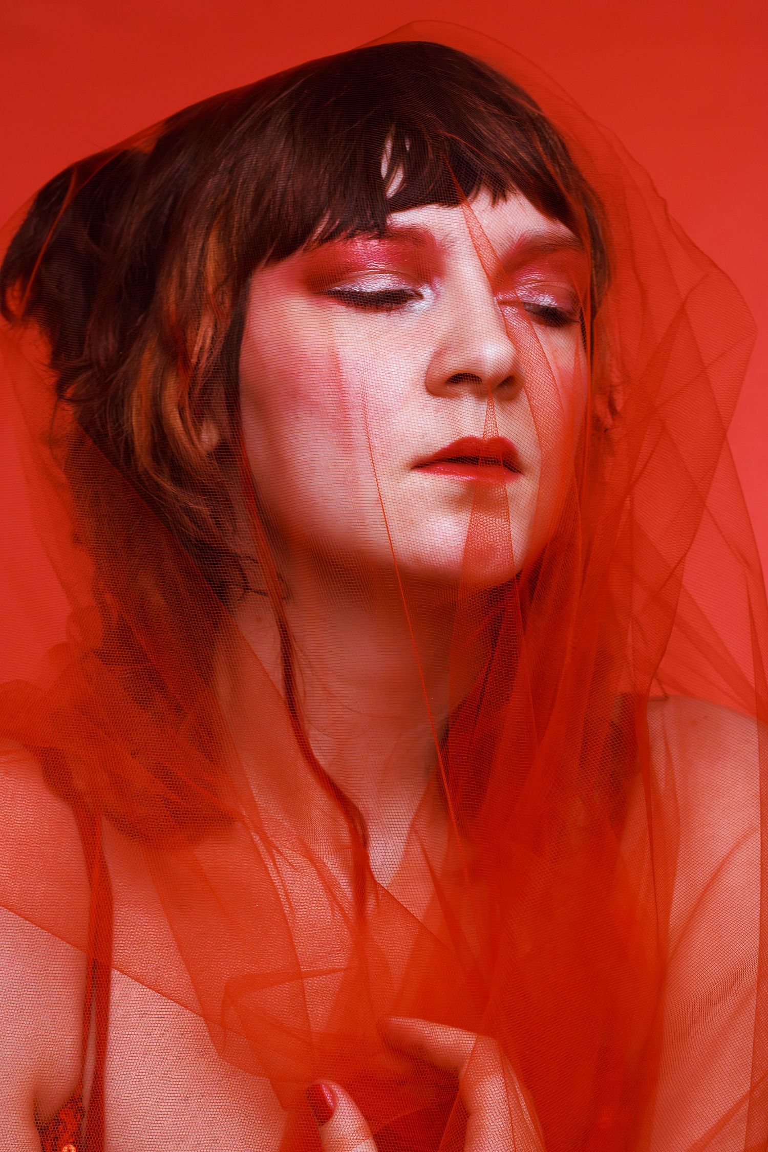 Artistic portrait of a woman with red makeup and sheer red veil on a red background, conceptual fine art photography by Sixtwentytwo Images.