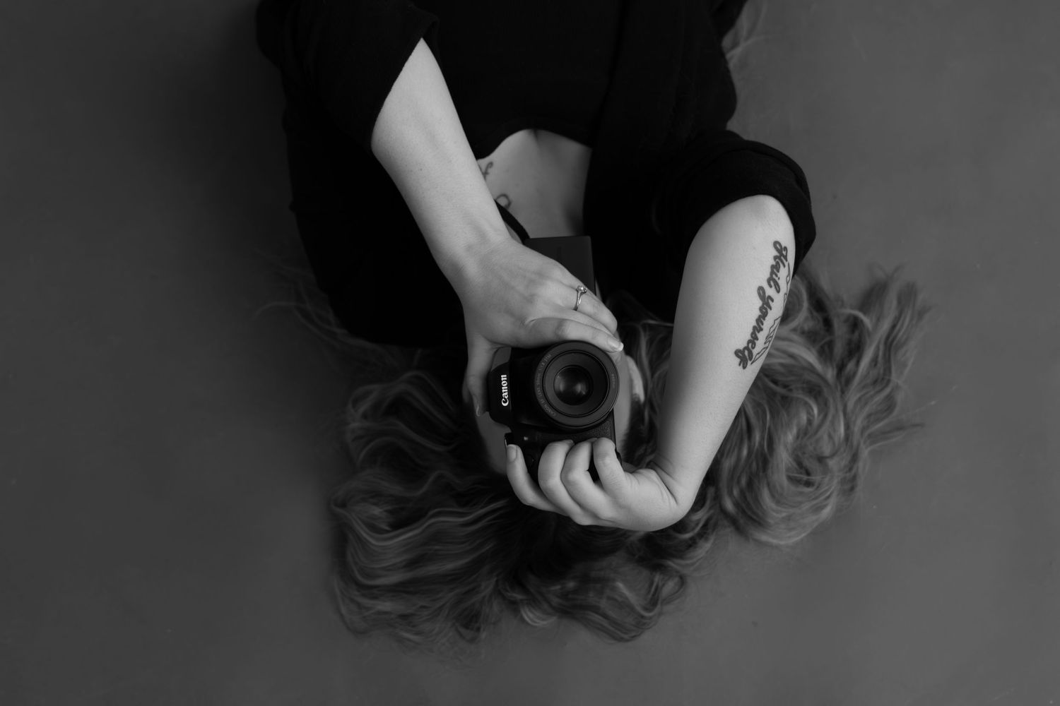 Artistic black and white photo of Bree from Sixtwentytwo Images lying on studio floor with Canon DSLR. Creative personal branding photograph