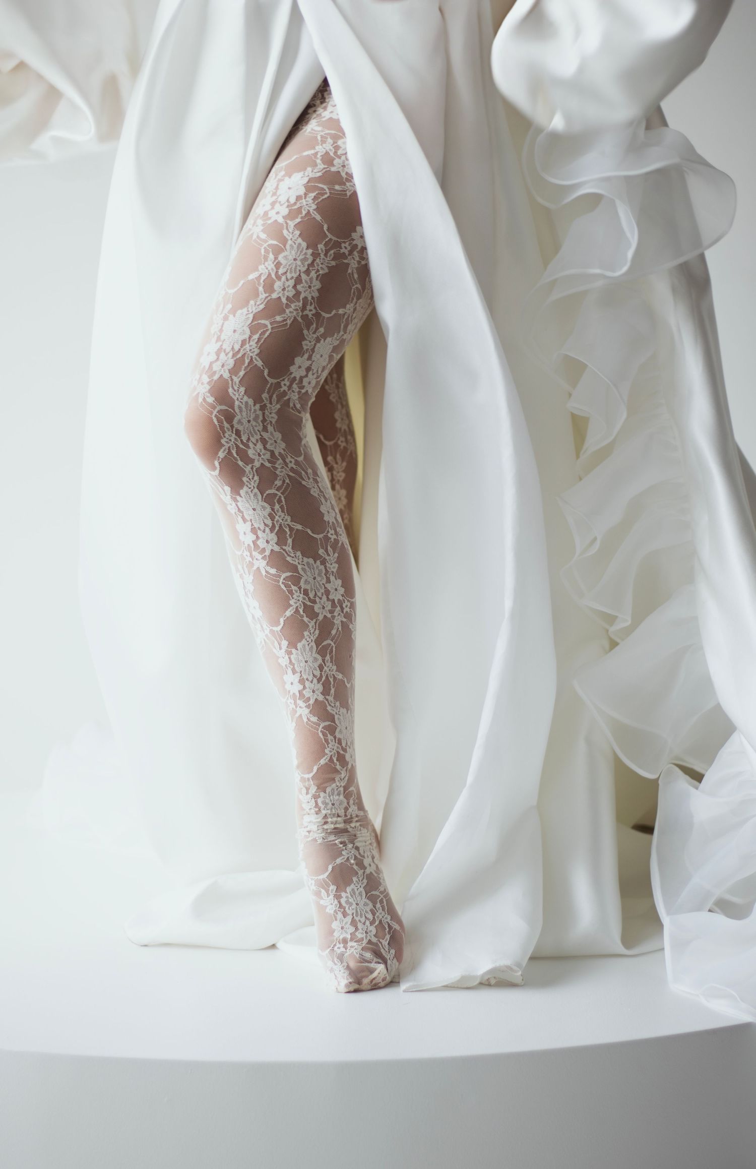 Editorial wedding photo showing lace stockings peeking through flowing white fabric at a professional studio in Sioux Falls, SD.