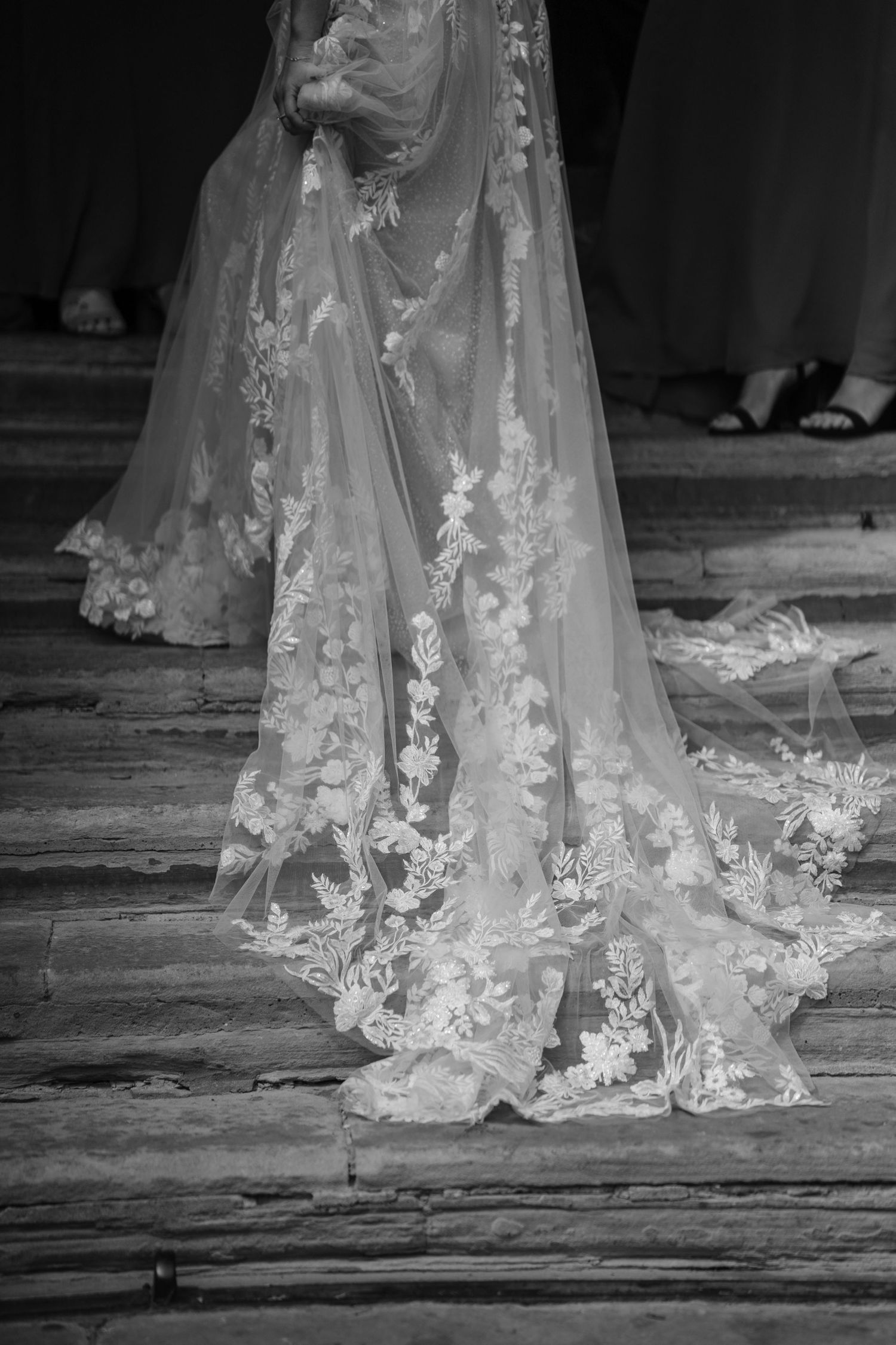Detailed lace embroidery adorns the trailing edge of a white wedding veil on stone steps.