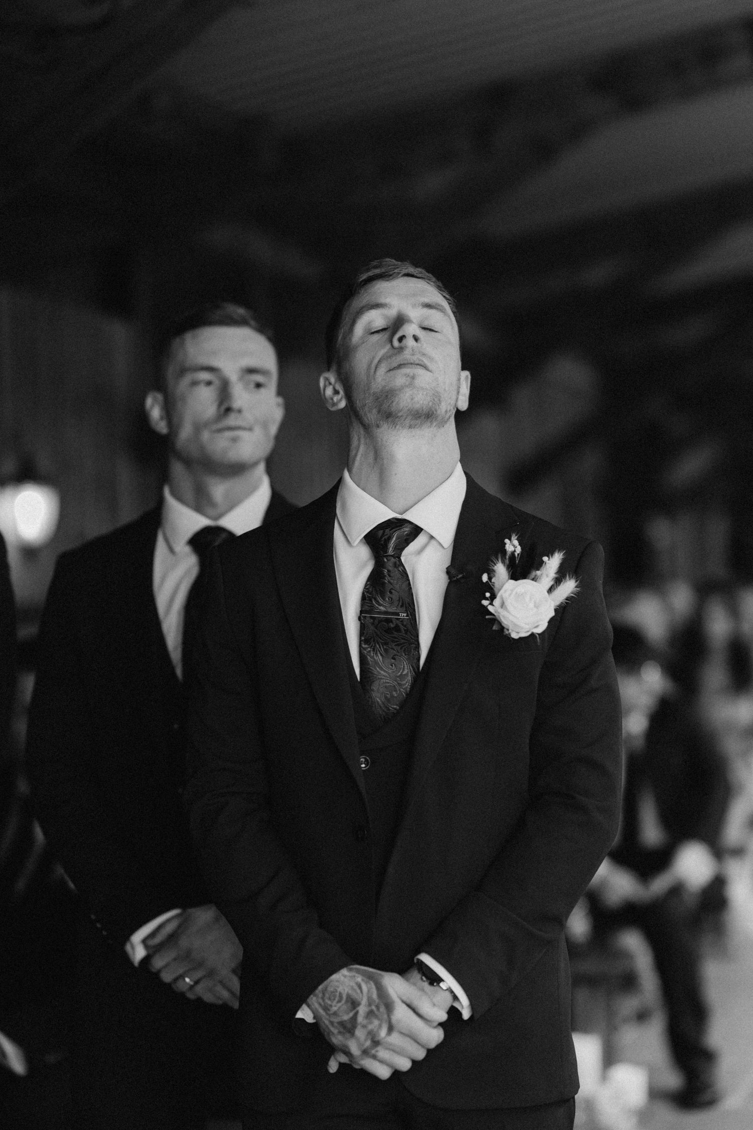 Black and white portrait of two men in formal suits at evening wedding celebration.