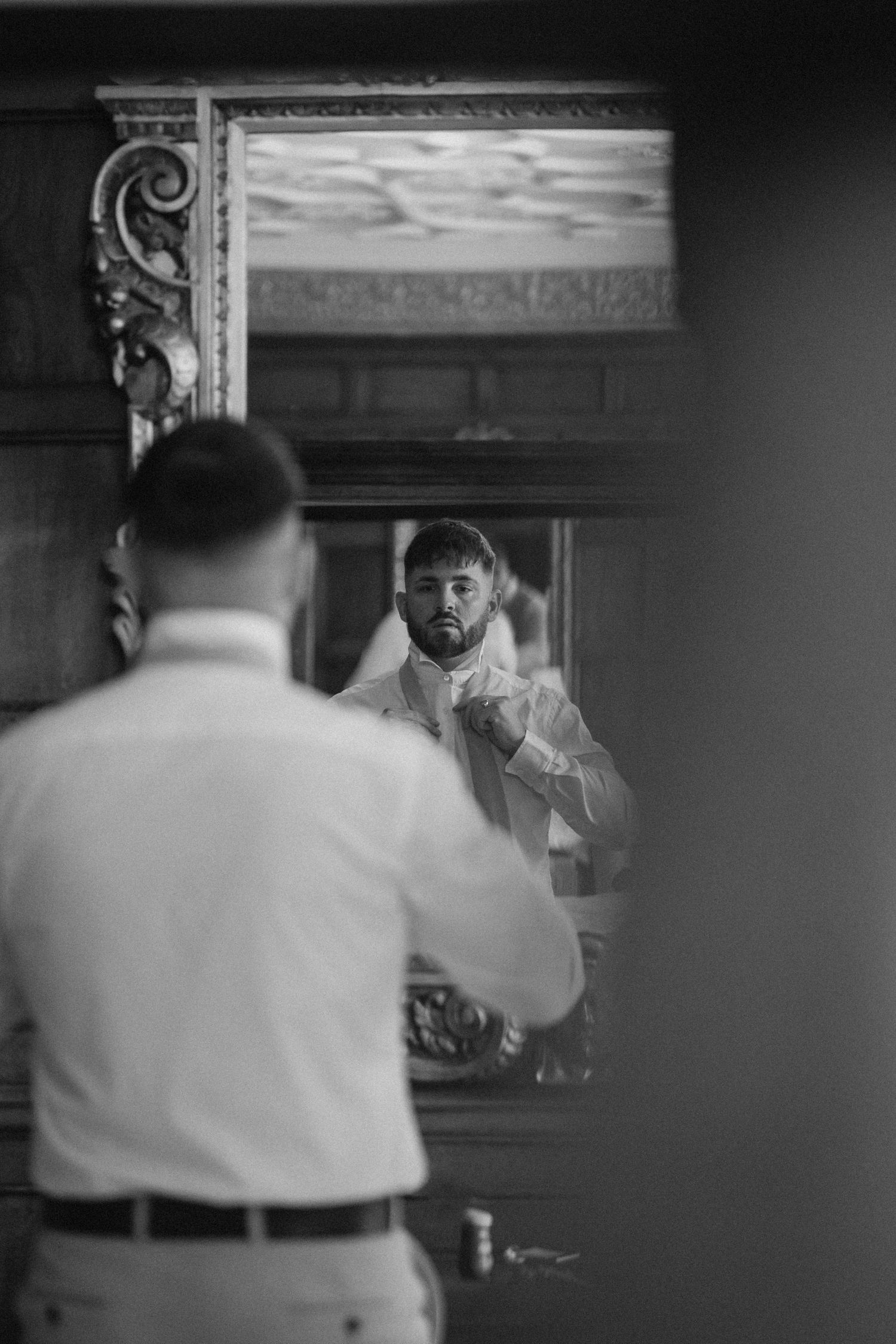 A black and white reflection in an ornate mirror while getting ready. Wedding photography at Rushton Hall