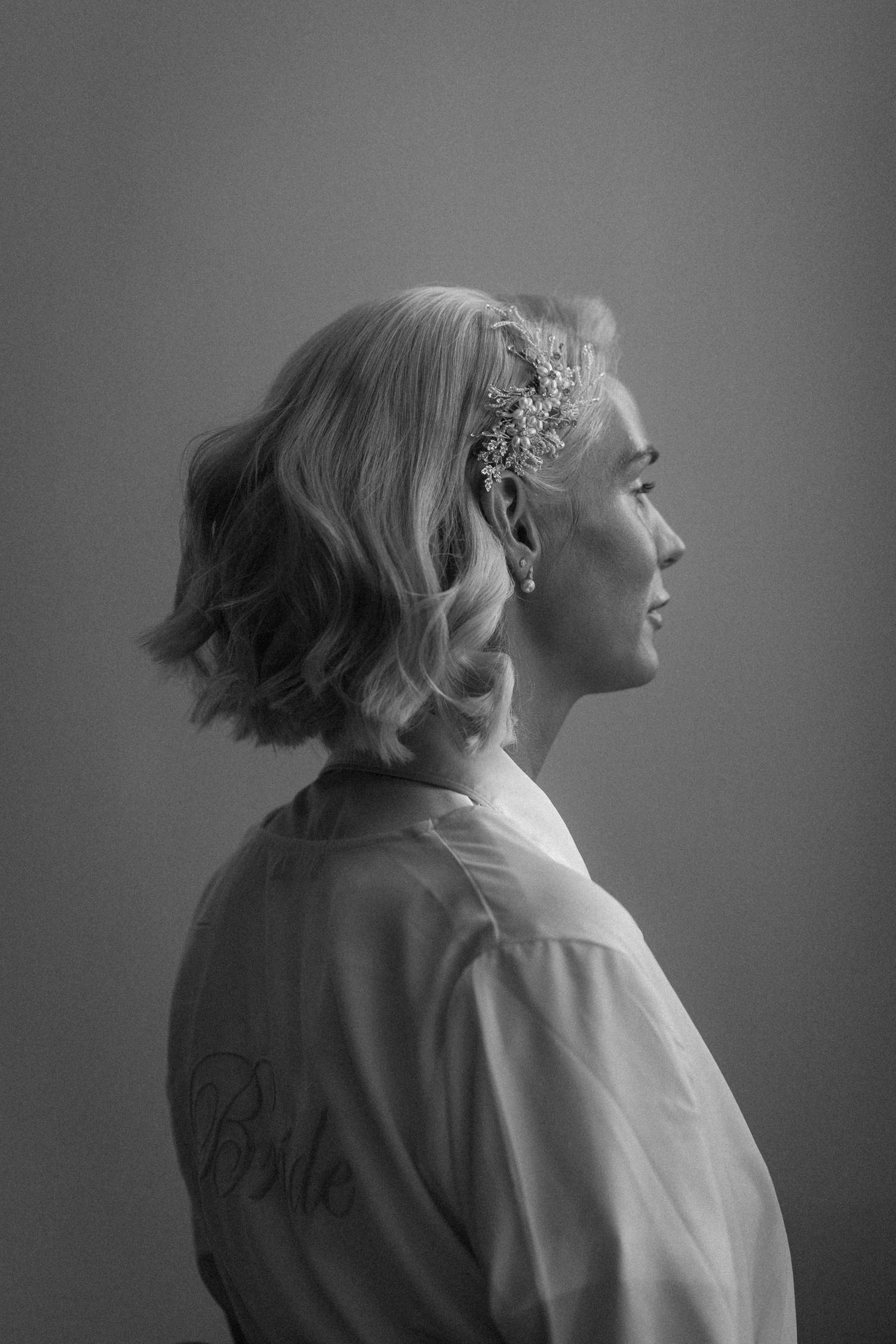 Black and white profile portrait of a bride with floral hair accessory wearing a satin robe.