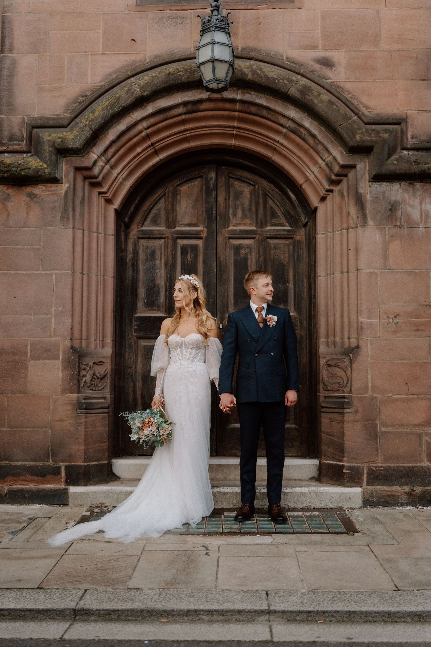 Newlyweds stand in front of ornate church doorway during their wedding photoshoot.