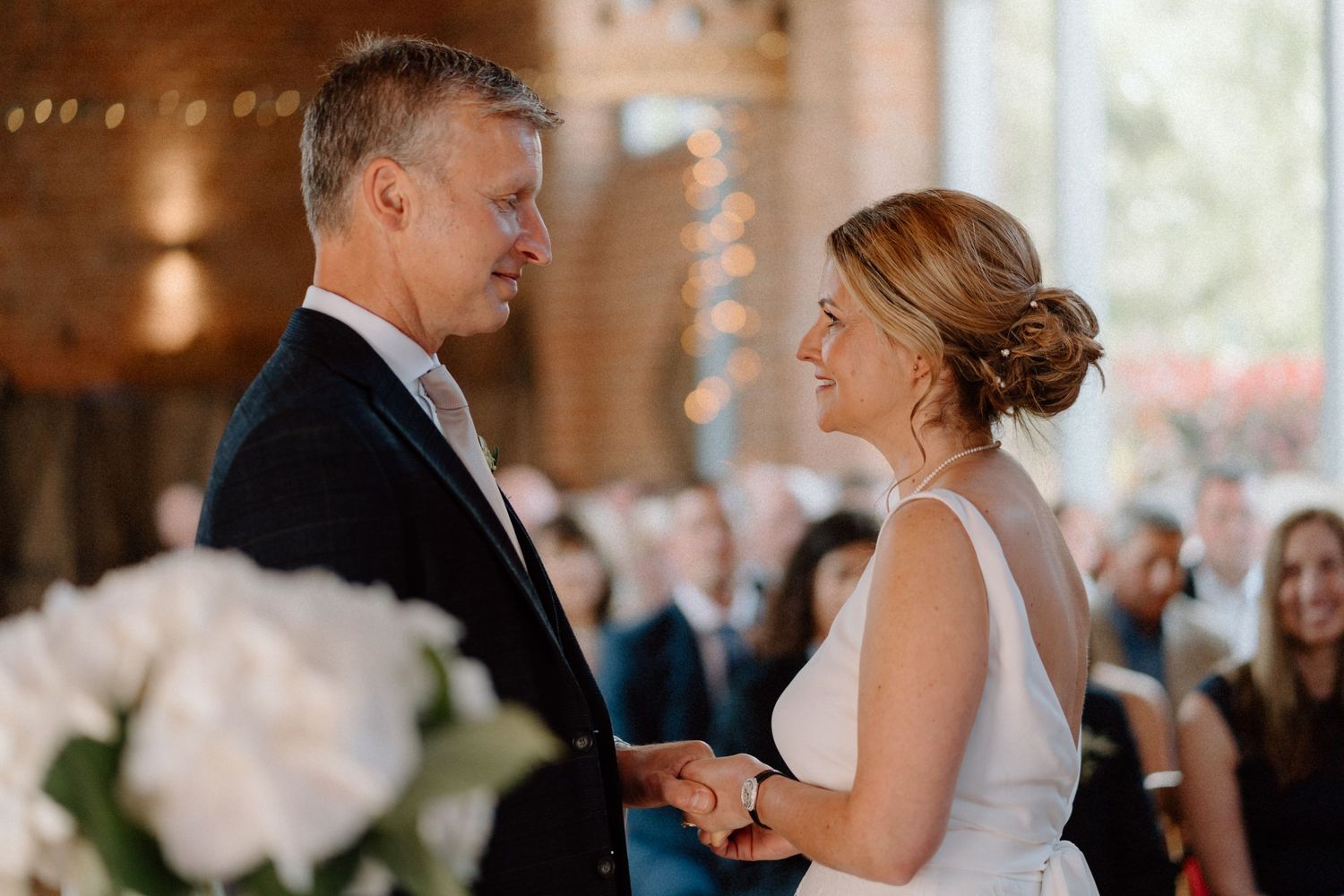 A romantic moment between newlyweds sharing their first dance at an indoor wedding reception with soft lighting at Swallows Nest Barn.