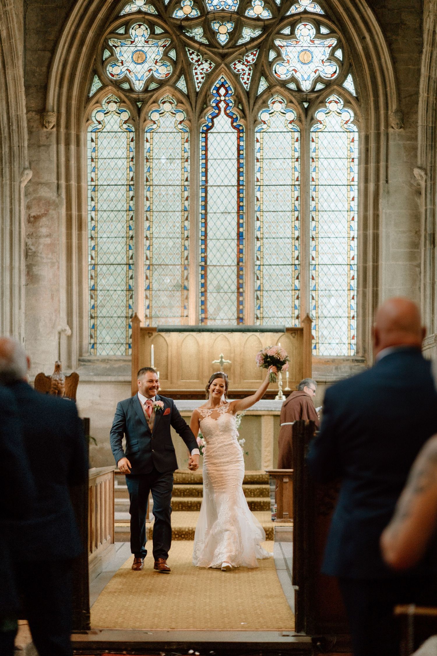 A joyful couple celebrates in a historic church with beautiful stained glass windows and stone architecture.